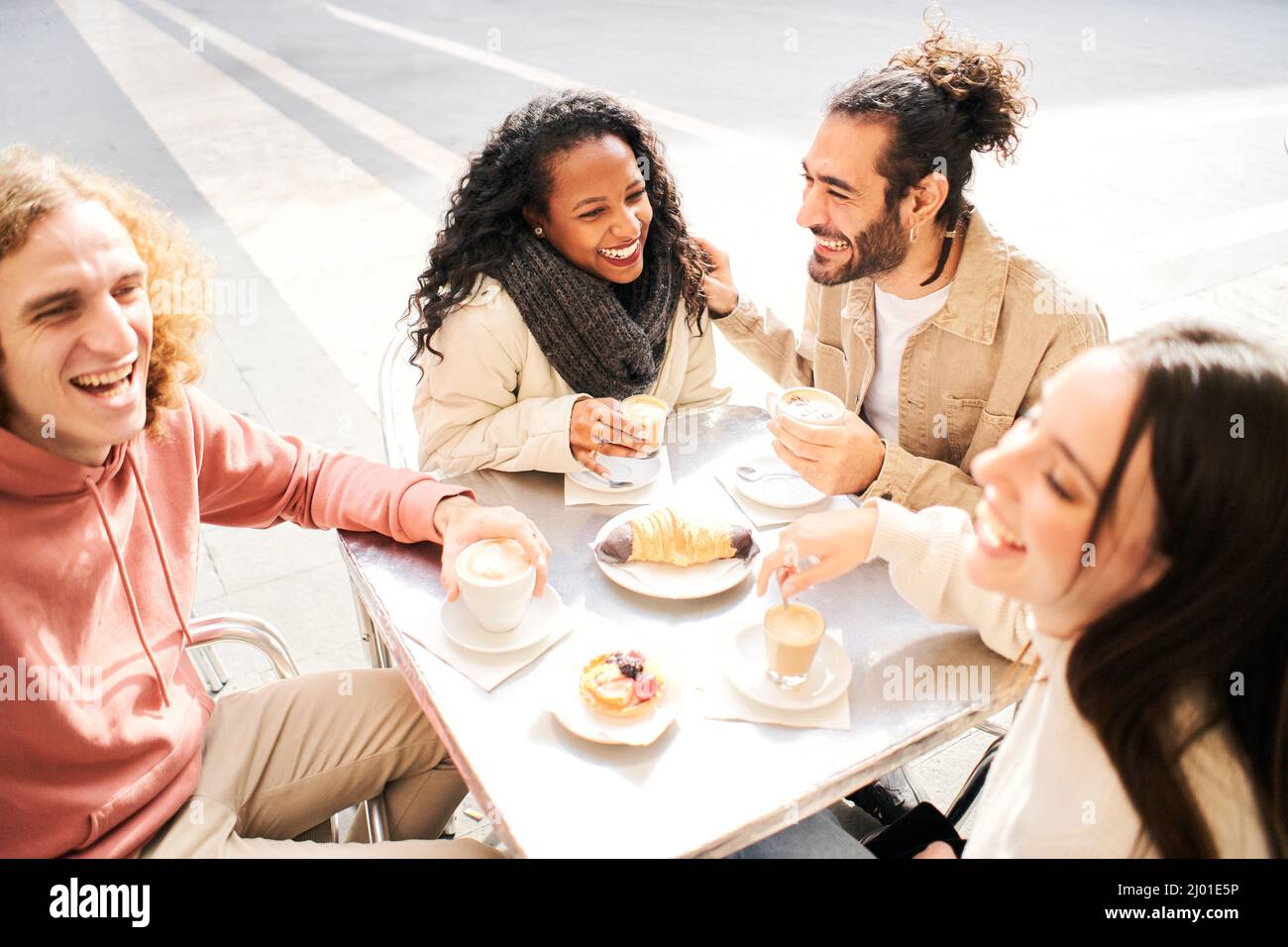 Gruppo di giovani multirazziali che fanno colazione in una caffetteria all'aperto. Studenti di diversi paesi che si divertono insieme bevendo caffè e. Foto Stock