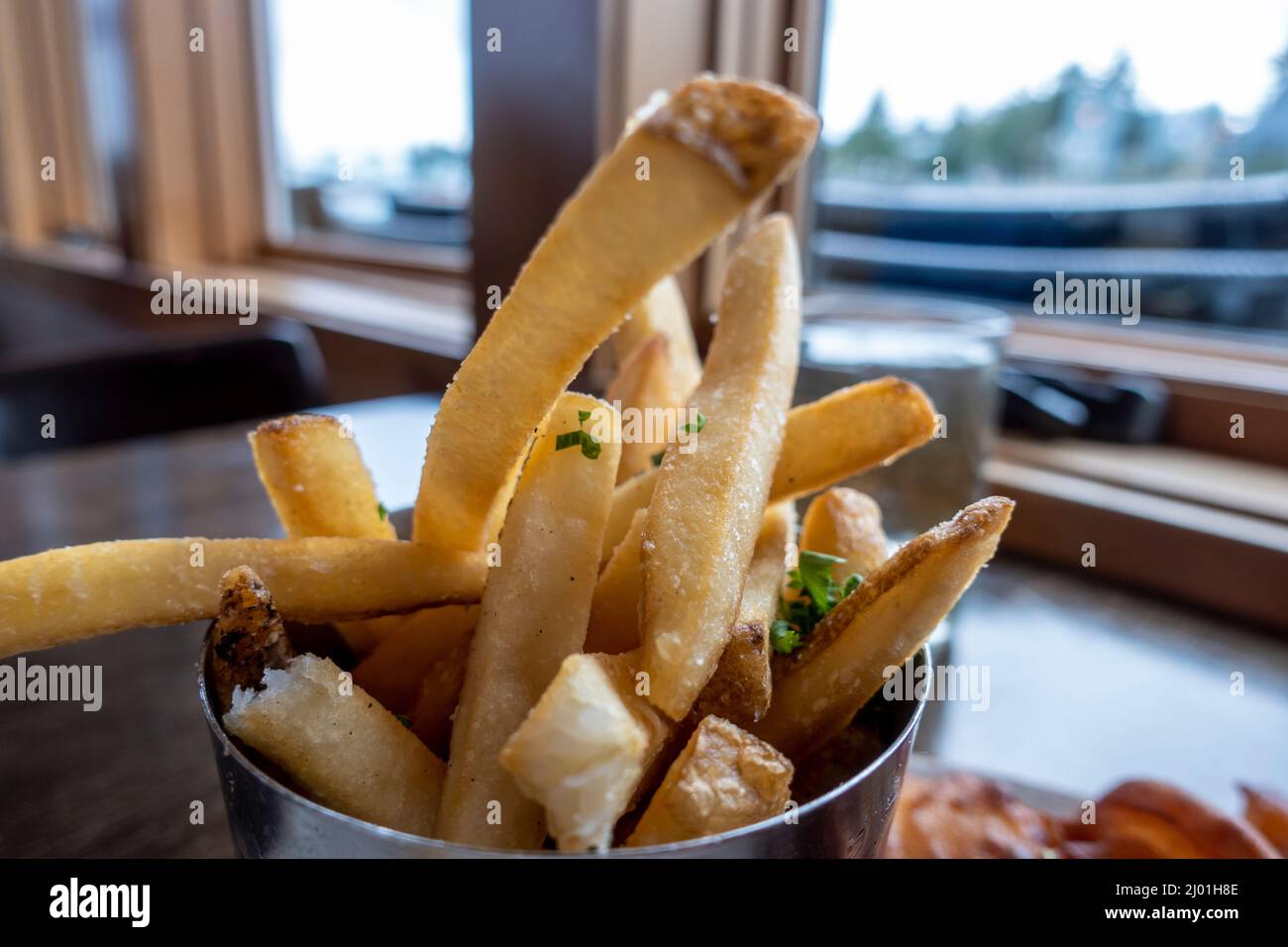 Primo piano, macro focus selettivo su patatine fritte croccanti con soffici centri di patate, presentato all'interno di una tazza di metallo in un ristorante interno Foto Stock