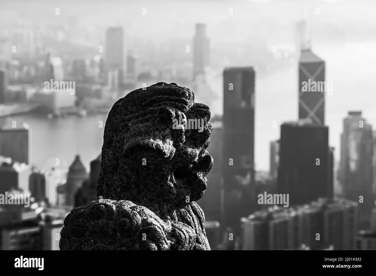 Una statua di leone di pietra si erge alla guardia del Padiglione del Leone, il picco, Hong Kong. L'iconico edificio della Banca della Cina è sullo sfondo Foto Stock