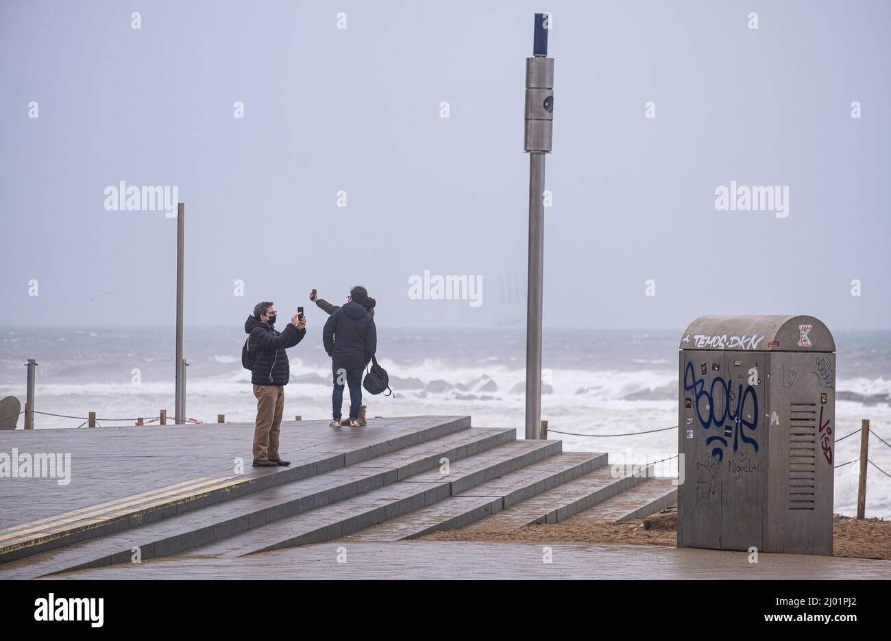 Barcellona, Spagna. 15th Mar 2022. Diverse persone si divertono mentre si scattano foto e si selfie durante la tempesta di mare. Barcellona soffre per il secondo giorno il flagello di una tempesta di mare battezzata come tempesta Celia. Nonostante il maltempo, i cittadini e i visitatori godono del forte vento e delle alte onde sulle spiagge di Barcellona. Credit: SOPA Images Limited/Alamy Live News Foto Stock