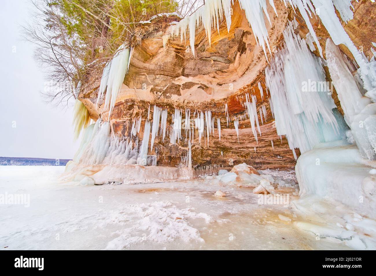 Caverna ondulata sulla scogliera sul lago ghiacciato coperto di ghiaccioli appuntiti Foto Stock