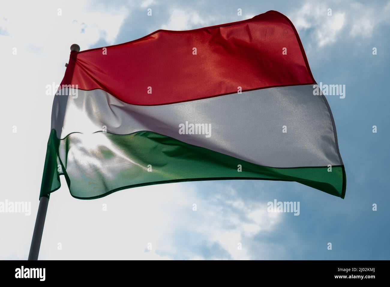 Bandiera ungherese che sventola sotto il vento e la luce del sole. Bandiera dell'Ungheria su sfondo cielo blu. Foto Stock