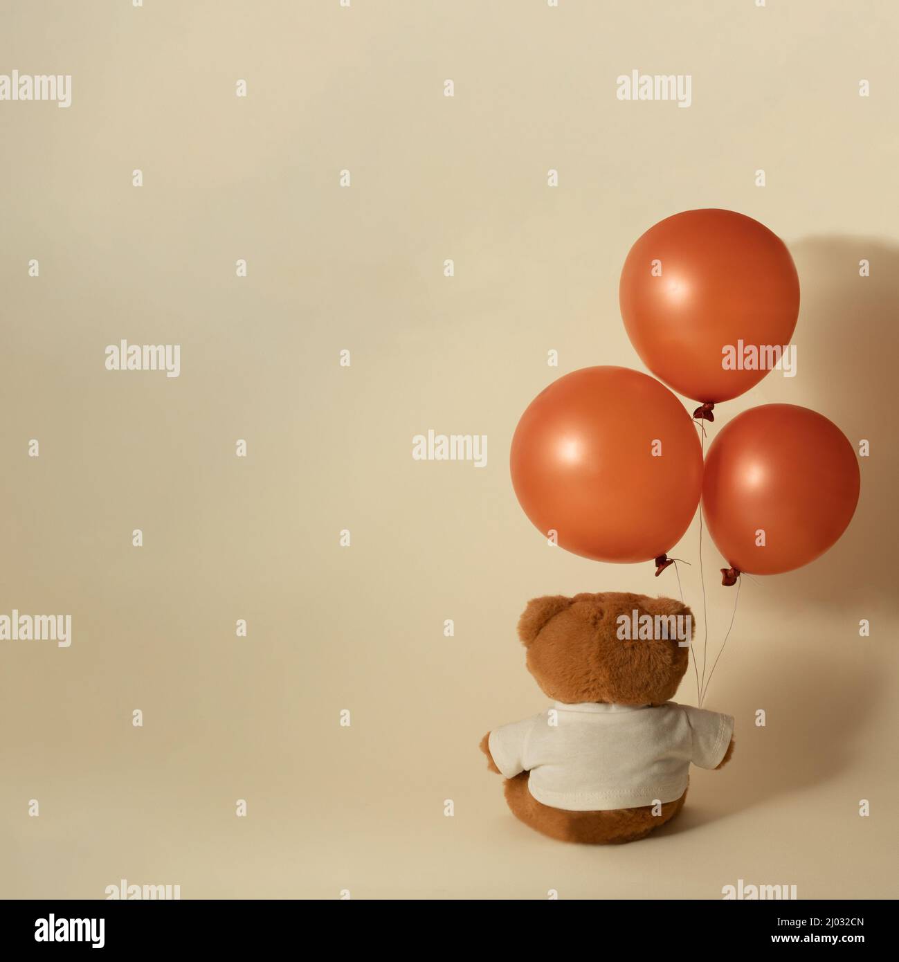 Piccolo orsacchiotto marrone giocattolo seduto e tenendo tre palloncini volanti su sfondo beige minimo. Foto Stock