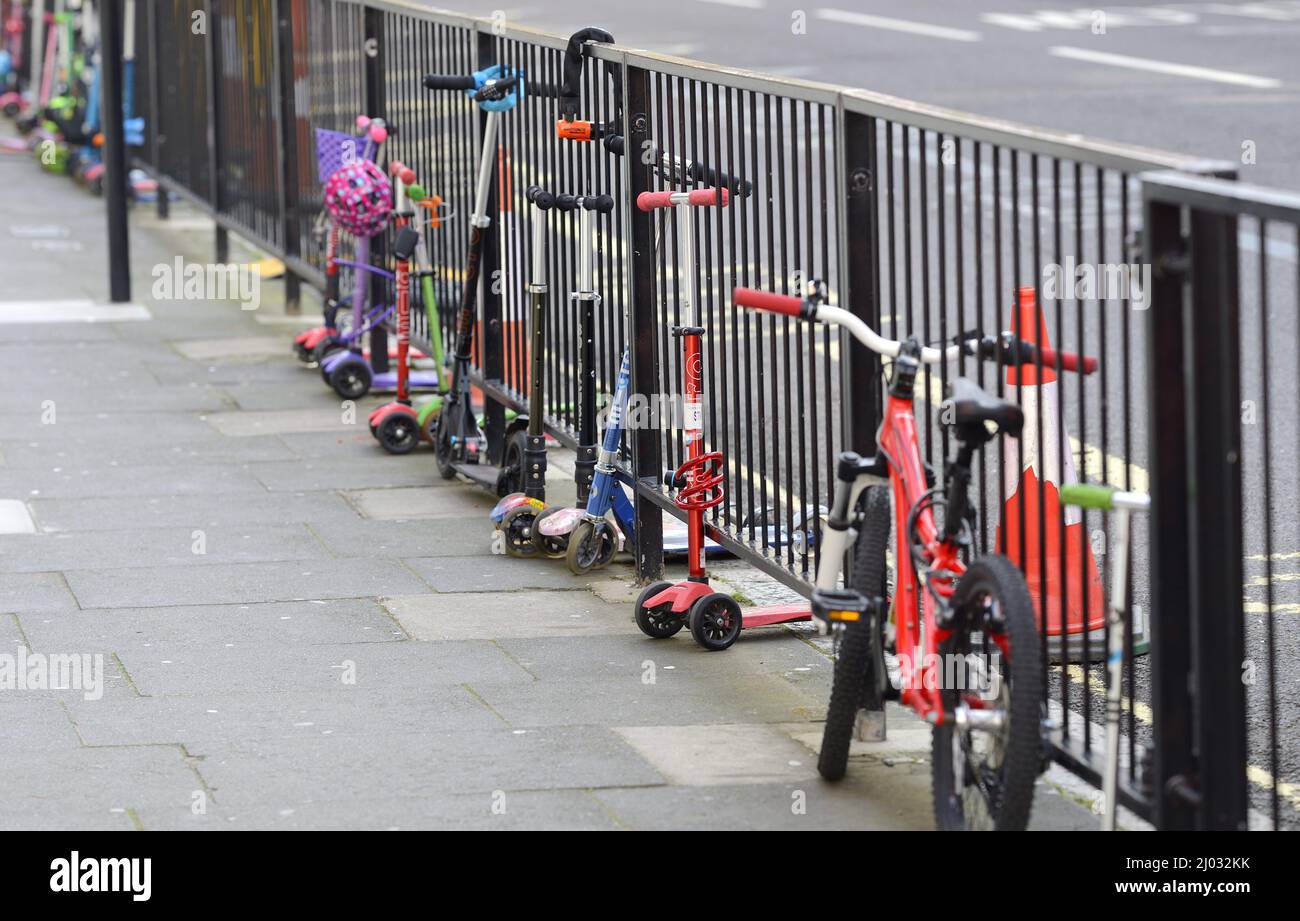 Londra, Inghilterra, Regno Unito. Gli scooter per bambini incatenavano a ringhiere fuori da una scuola elementare Foto Stock