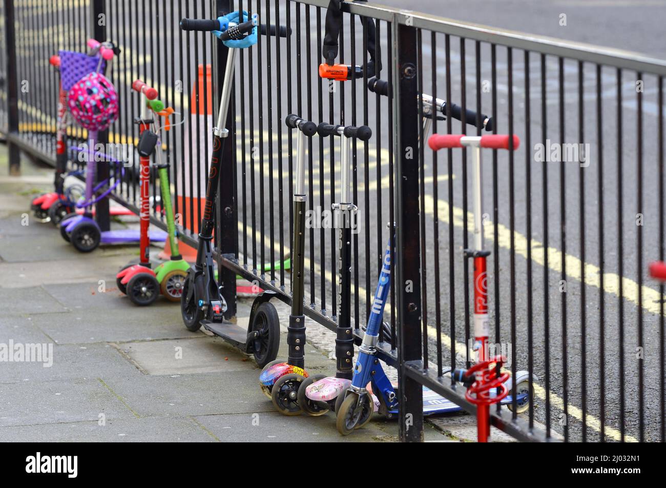 Londra, Inghilterra, Regno Unito. Gli scooter per bambini incatenavano a ringhiere fuori da una scuola elementare Foto Stock