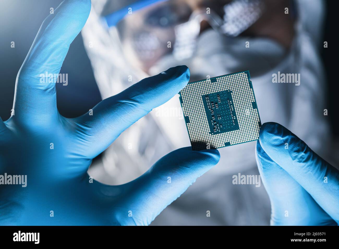 In Ultra Modern Electronic Manufacturing Factory Design Engineer in Sterile Coverall tiene Microchip con guanti ed esamina Foto Stock