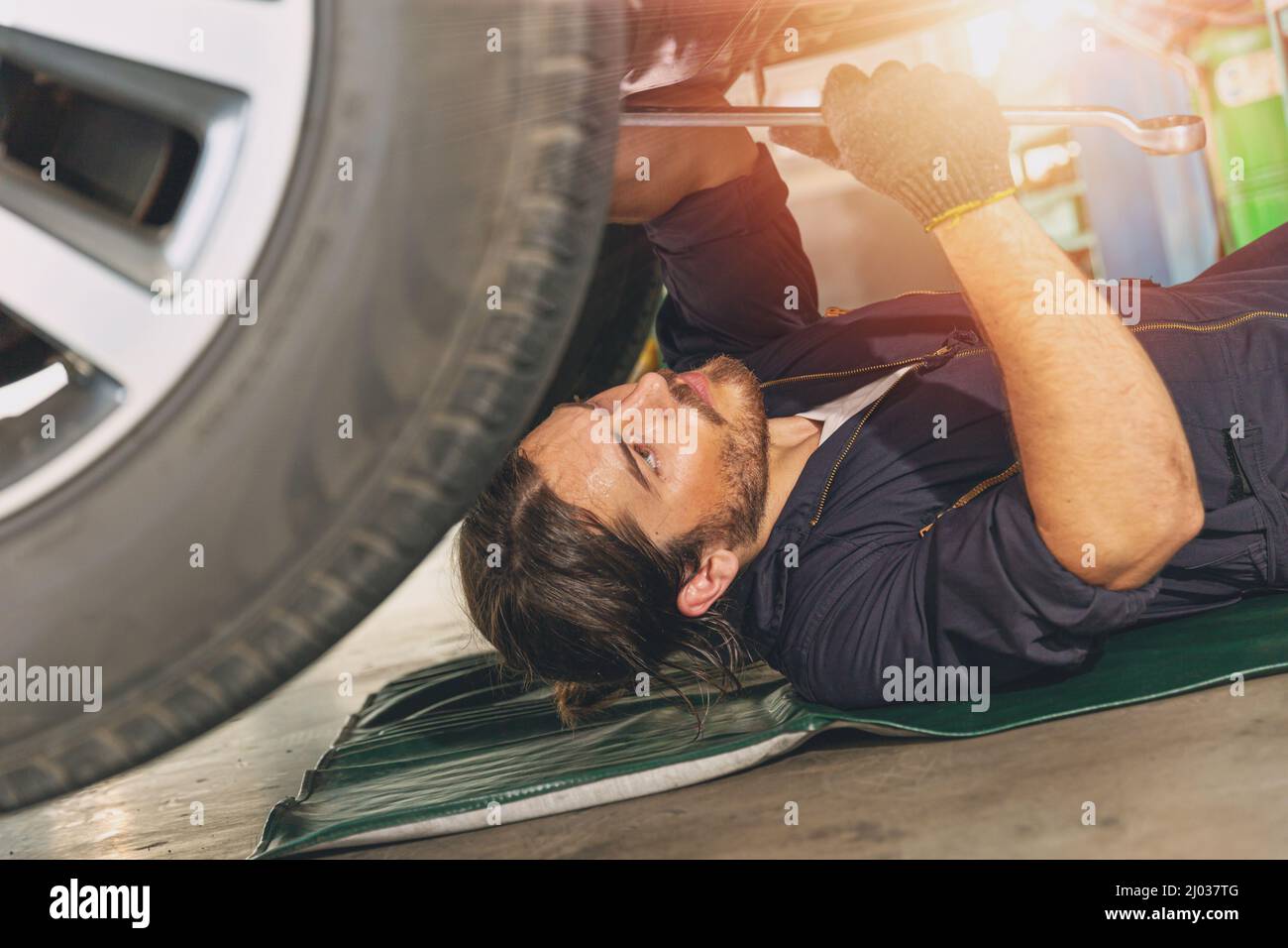 Il personale meccanico che lavora sotto l'auto ripara e ripara le sospensioni degli pneumatici in garage Foto Stock