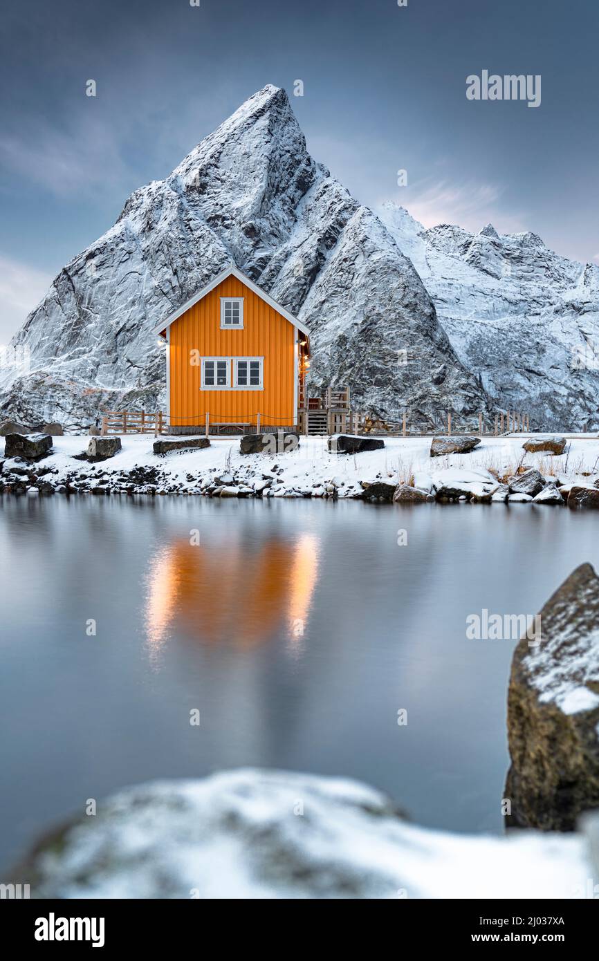Rorbu nella neve ai piedi del monte Olstind che si affaccia sul Mare Artico, Sakrisoy, Reine, Nordland, Isole Lofoten, Norvegia, Scandinavia, Europa Foto Stock