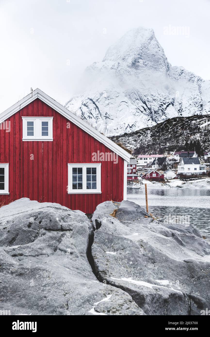 Rorbu rosso nel paesaggio ghiacciato con il monte Olstind innevato sullo sfondo, Reine, Nordland, Isole Lofoten, Norvegia, Scandinavia, Europa Foto Stock
