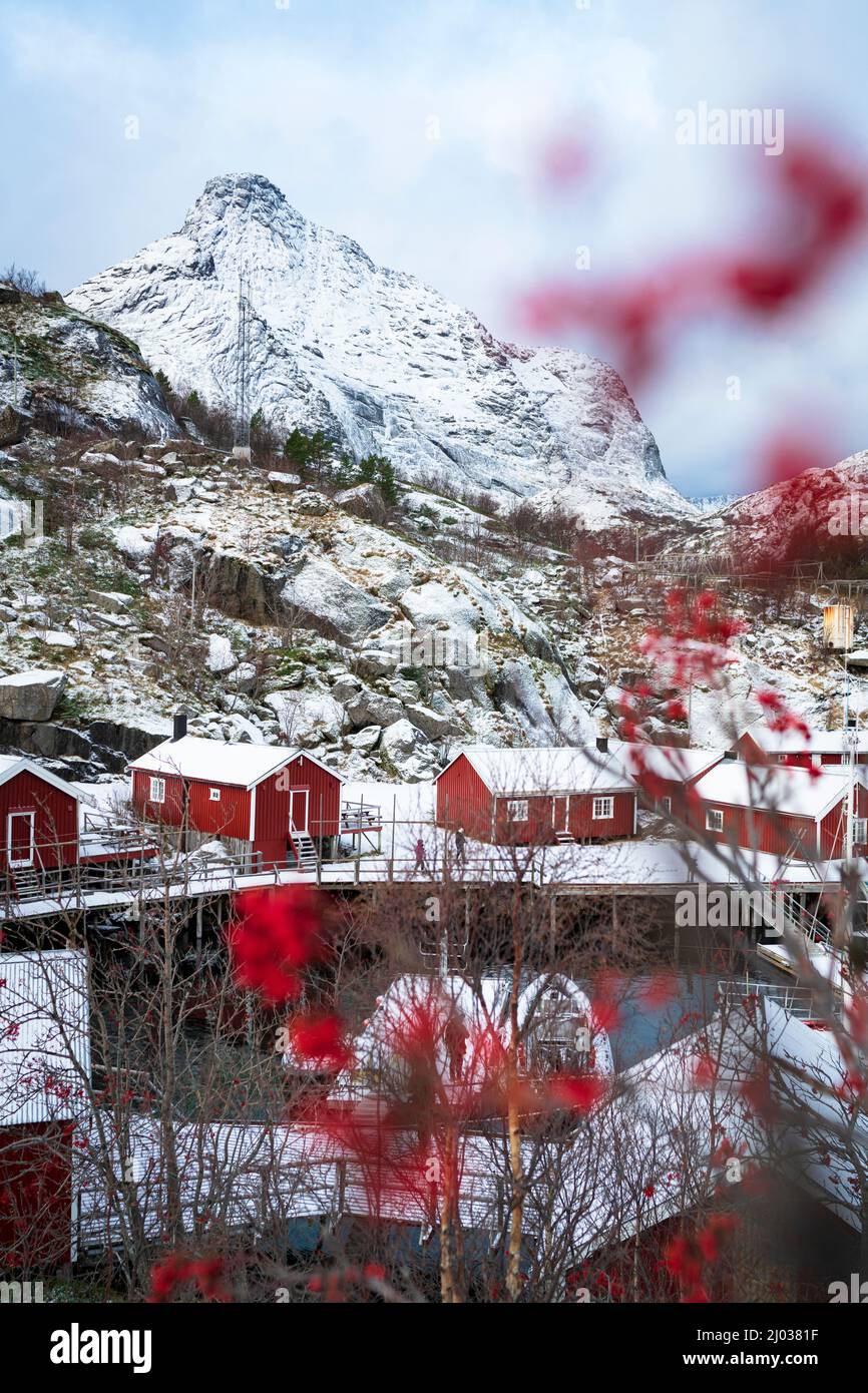 Cabine rosse di Rorbu incorniciate da montagne innevate in inverno, Nusfjord, contea di Nordland, Isole Lofoten, Norvegia, Scandinavia, Europa Foto Stock