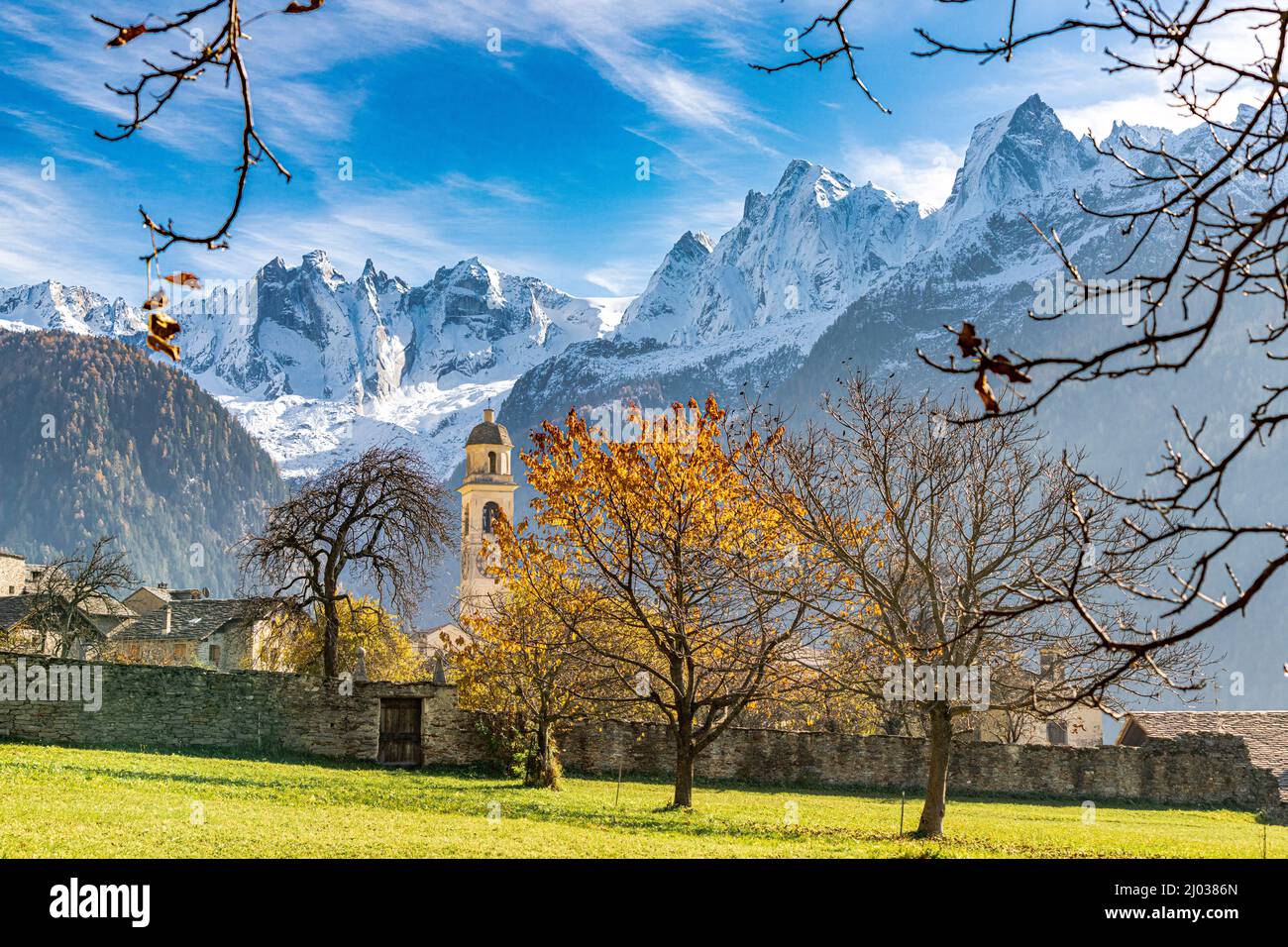 Vecchia chiesa illuminata dai colori autunnali con lo sfondo di Piz Badile e Cengalo innevato, Soglio, Graubunden, Svizzera, Europa Foto Stock