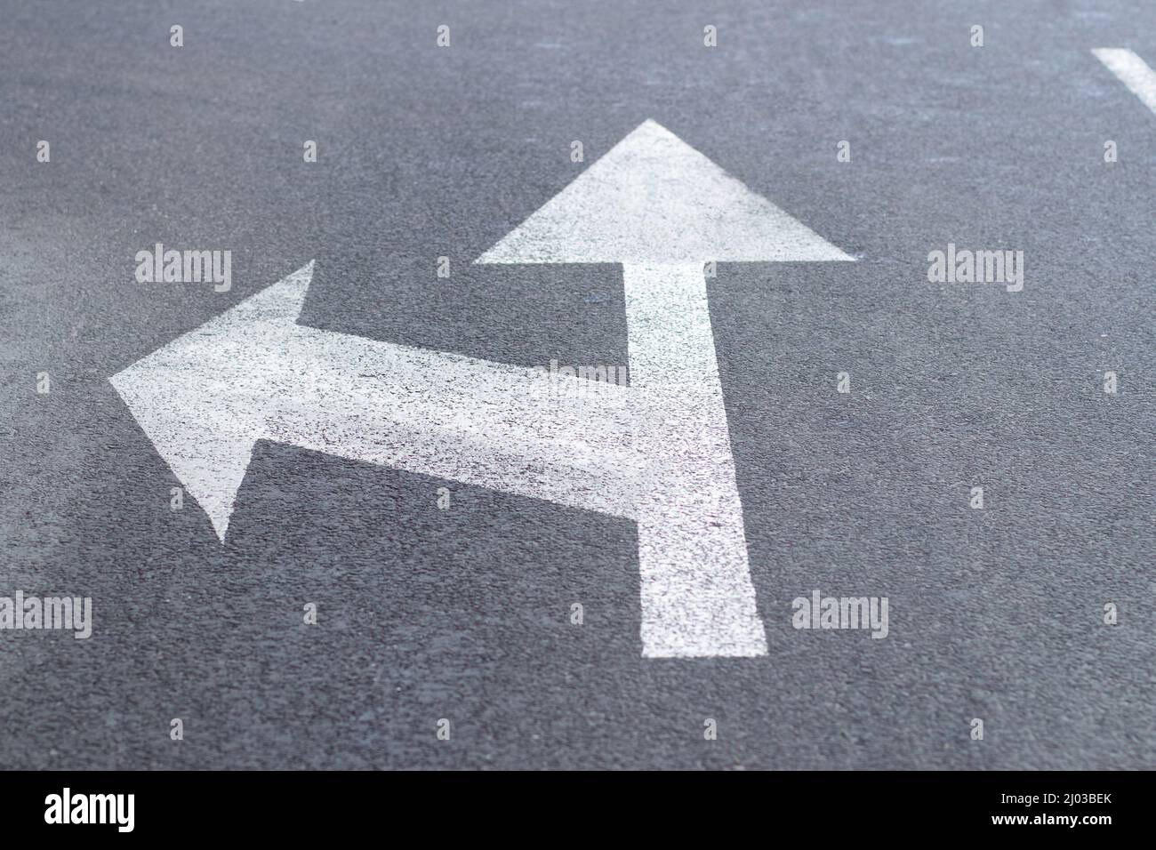Frecce di segnaletica stradale su una strada asfaltata per la direzione di movimento rettilinea o a sinistra Foto Stock