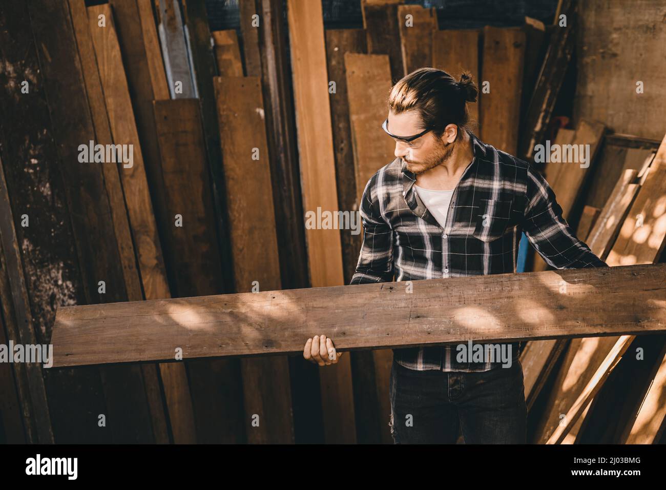 L'uomo carpentieri alto esperto legno che fa mobili. Maestro di legno maschio guardando il pannello di legno. Foto Stock
