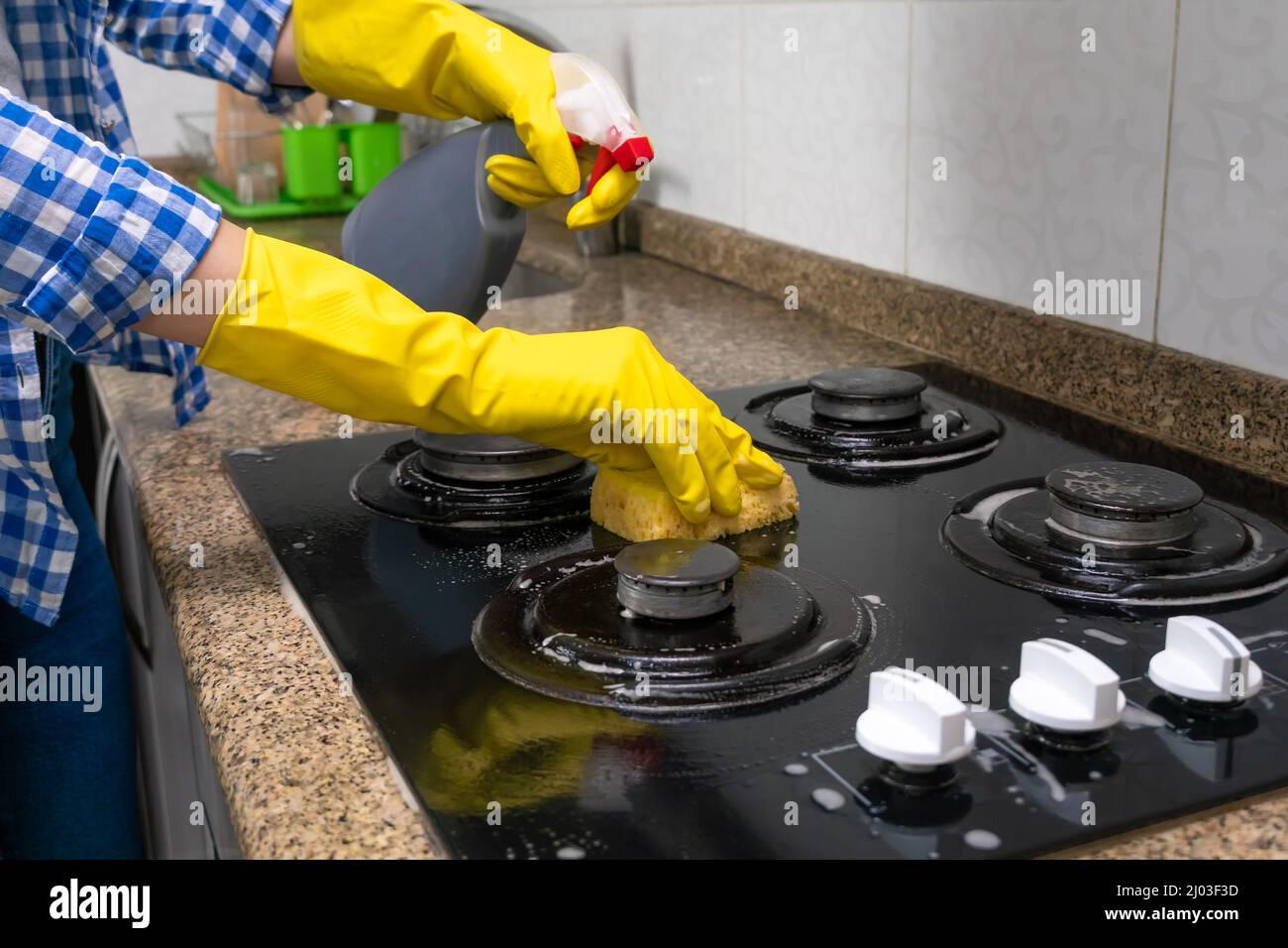Mano della donna in guanti gialli lavando il fornello della cucina con un agente pulente e una spugna Foto Stock