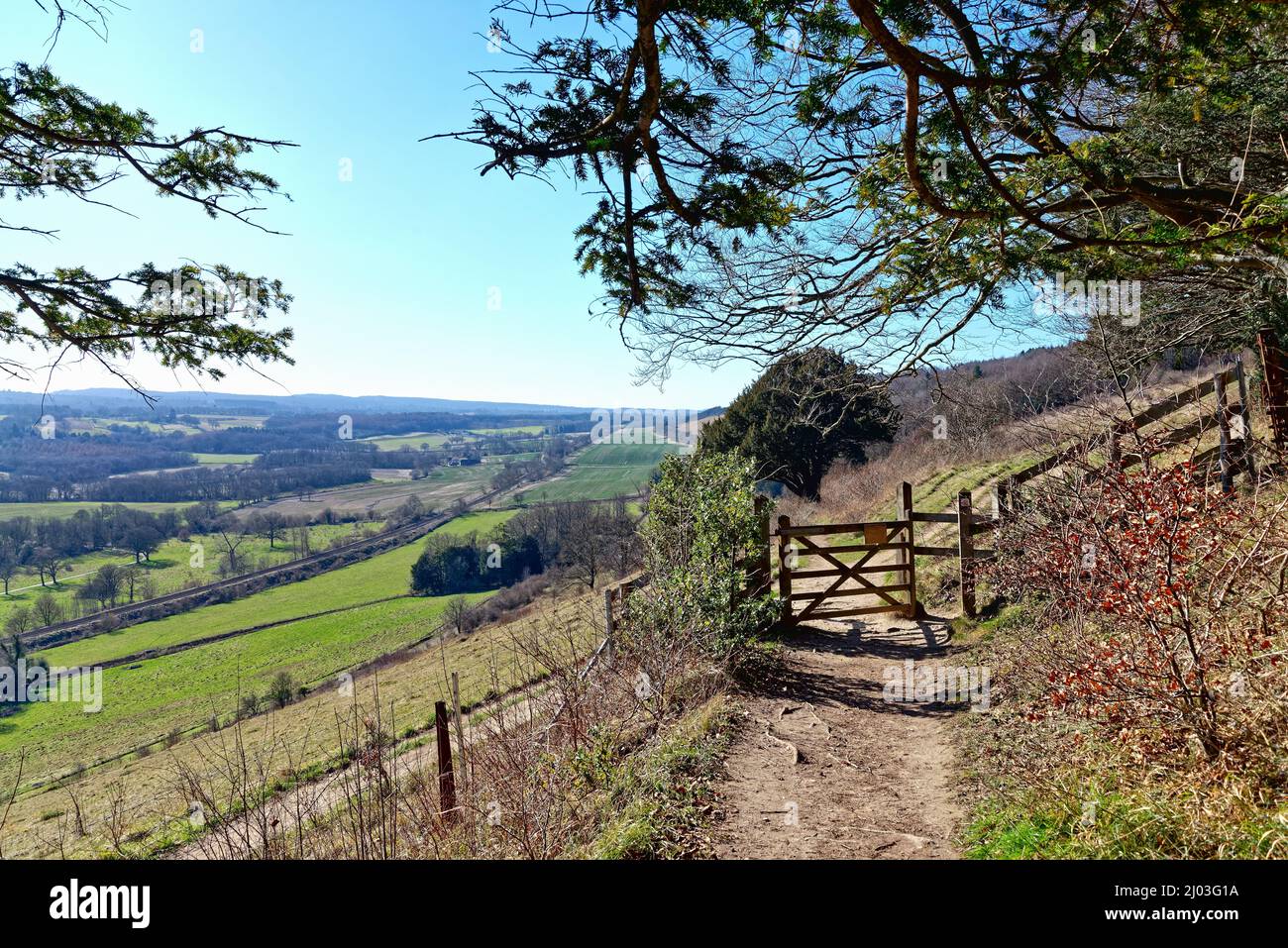 La vista che guarda ad ovest da Ranmore Common nelle Surrey Hills con un cancello di legno in primo piano in un giorno d'inverno soleggiato, Dorking Inghilterra UK Foto Stock