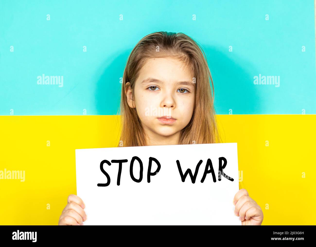 Una ragazza sta piangendo, tenendo in mano un manifesto DI FINE GUERRA contro lo sfondo della bandiera Ucraina. Fermare la guerra in Ucraina. Il concetto di pace Foto Stock