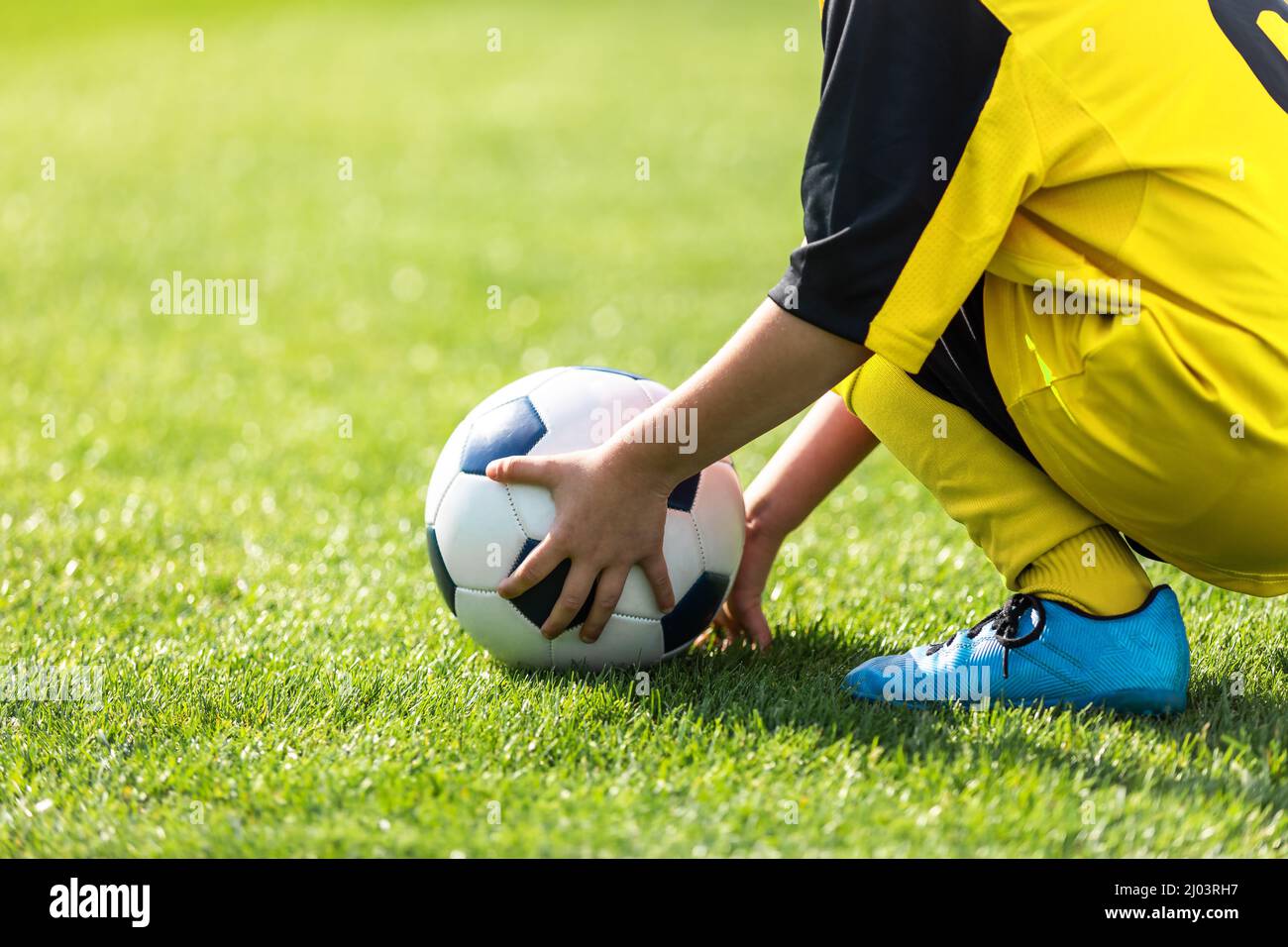 Il bambino prenda la sfera dal campo di gioco. Bambino che tiene la palla  di calcio in mano. Ragazzo in divisa da calcio e scarpe da gioco Foto stock  - Alamy