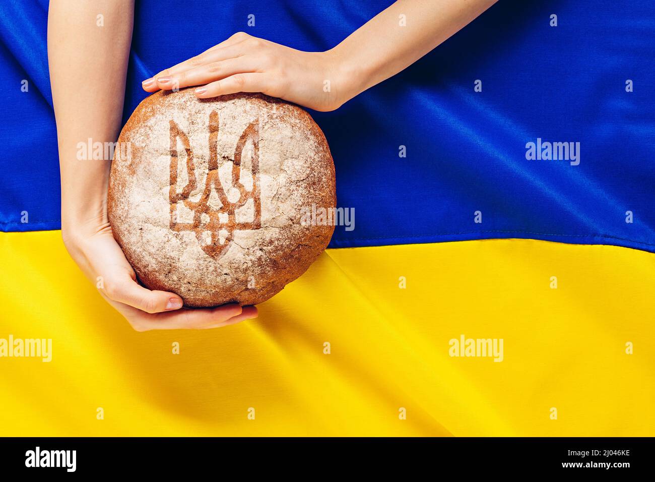 Pane nelle mani della donna con il mantello di armi dell'Ucraina sullo sfondo della bandiera Ucraina Foto Stock