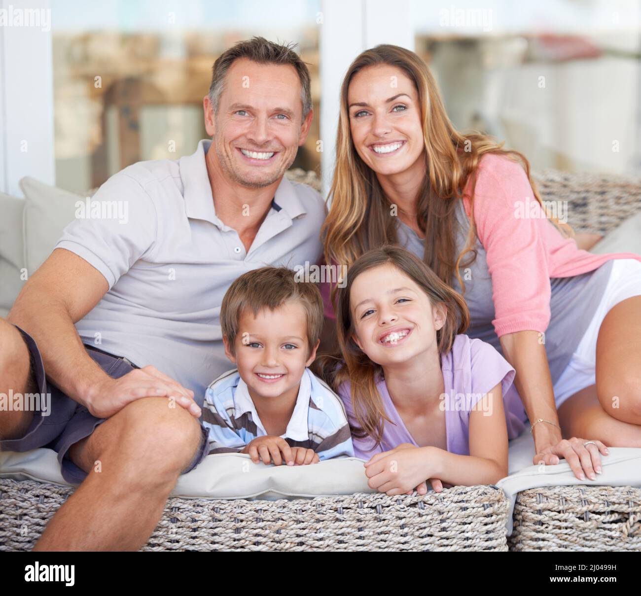 La famiglia è perfetta per le immagini. Ritratto di una giovane famiglia felice di quattro seduti insieme sul patio. Foto Stock