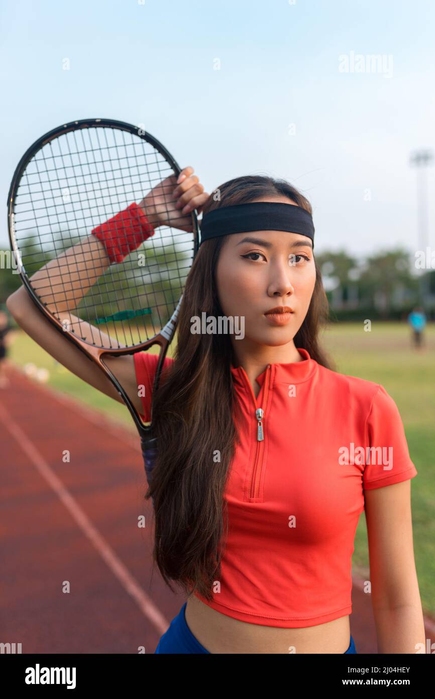 Giovane donna asiatica con fascia nera in piedi sul campo da tennis e con racchetta da tennis. Foto di alta qualità Foto Stock