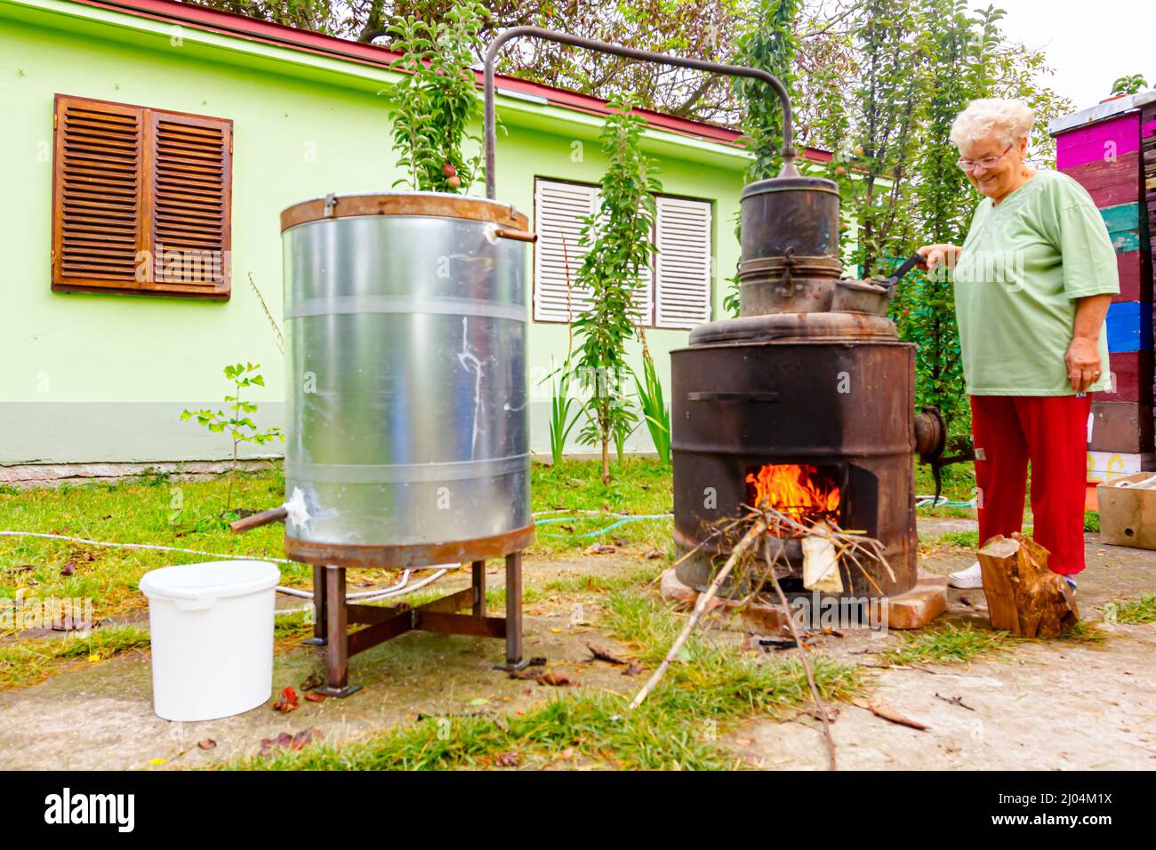 La donna sta girando manualmente la leva per mescolare le vinacce di frutta in caldaia di distilleria fatta in casa di rame, facendo schnapps moonshine, bevande alcoliche come Foto Stock