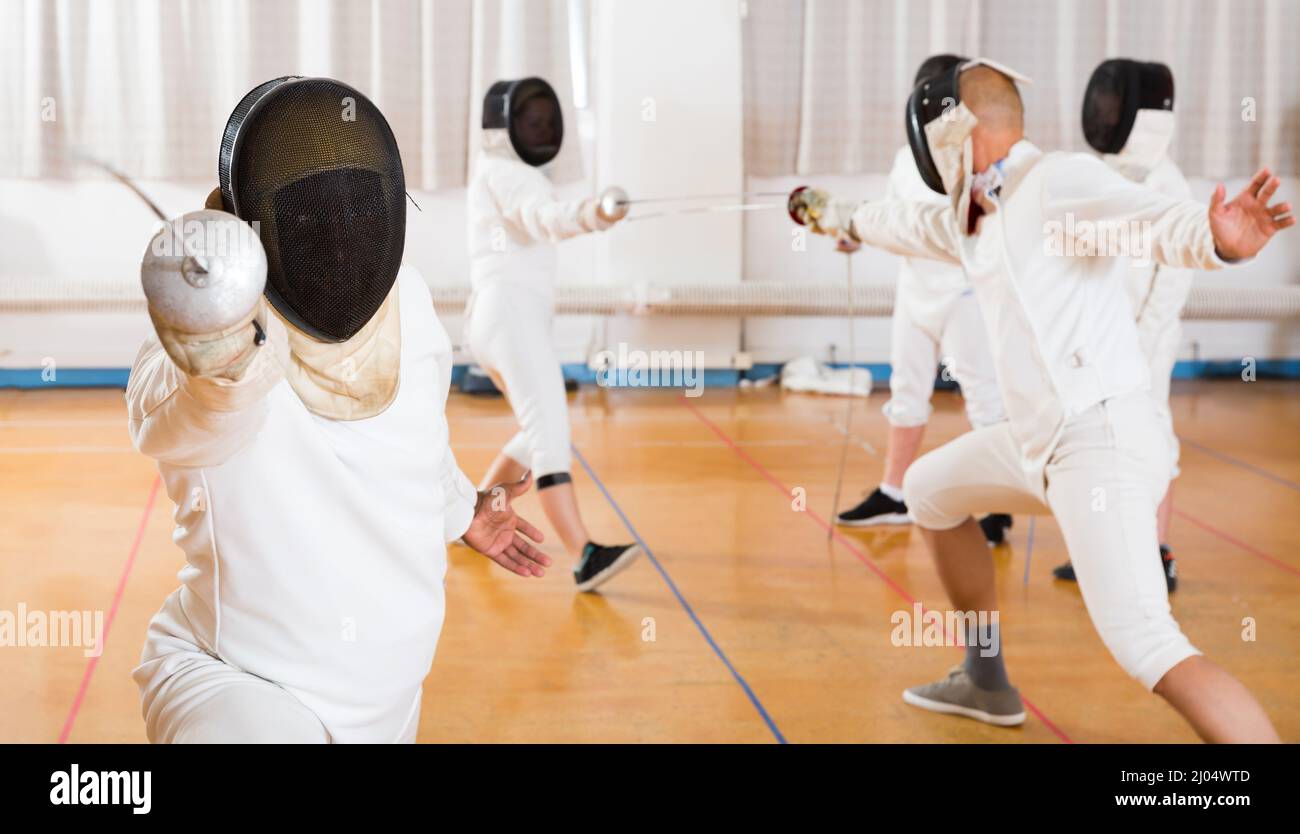 Closeup ritratto di fencer in maschera affondo praticante con un foglio di alluminio durante la scherma allenamento in palestra Foto Stock