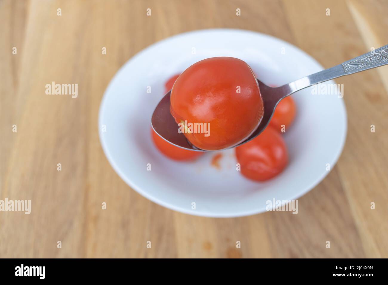 Primo piano di pomodori marinati in un piatto bianco con fondo in legno - un cucchiaio con pomodori. Foto Stock