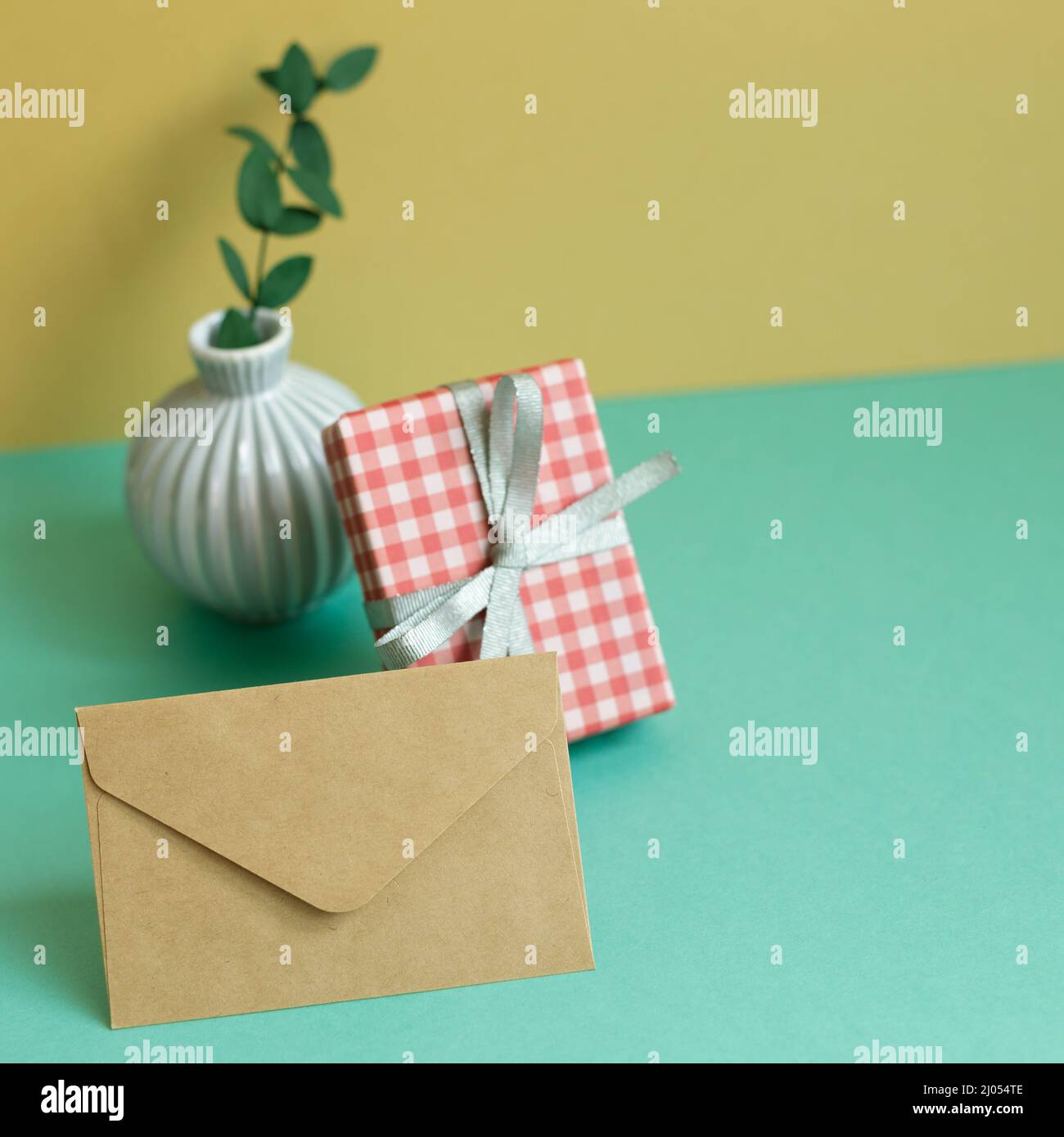 Confezione regalo, pianta, busta su tavola verde. Sfondo parete giallo Foto Stock