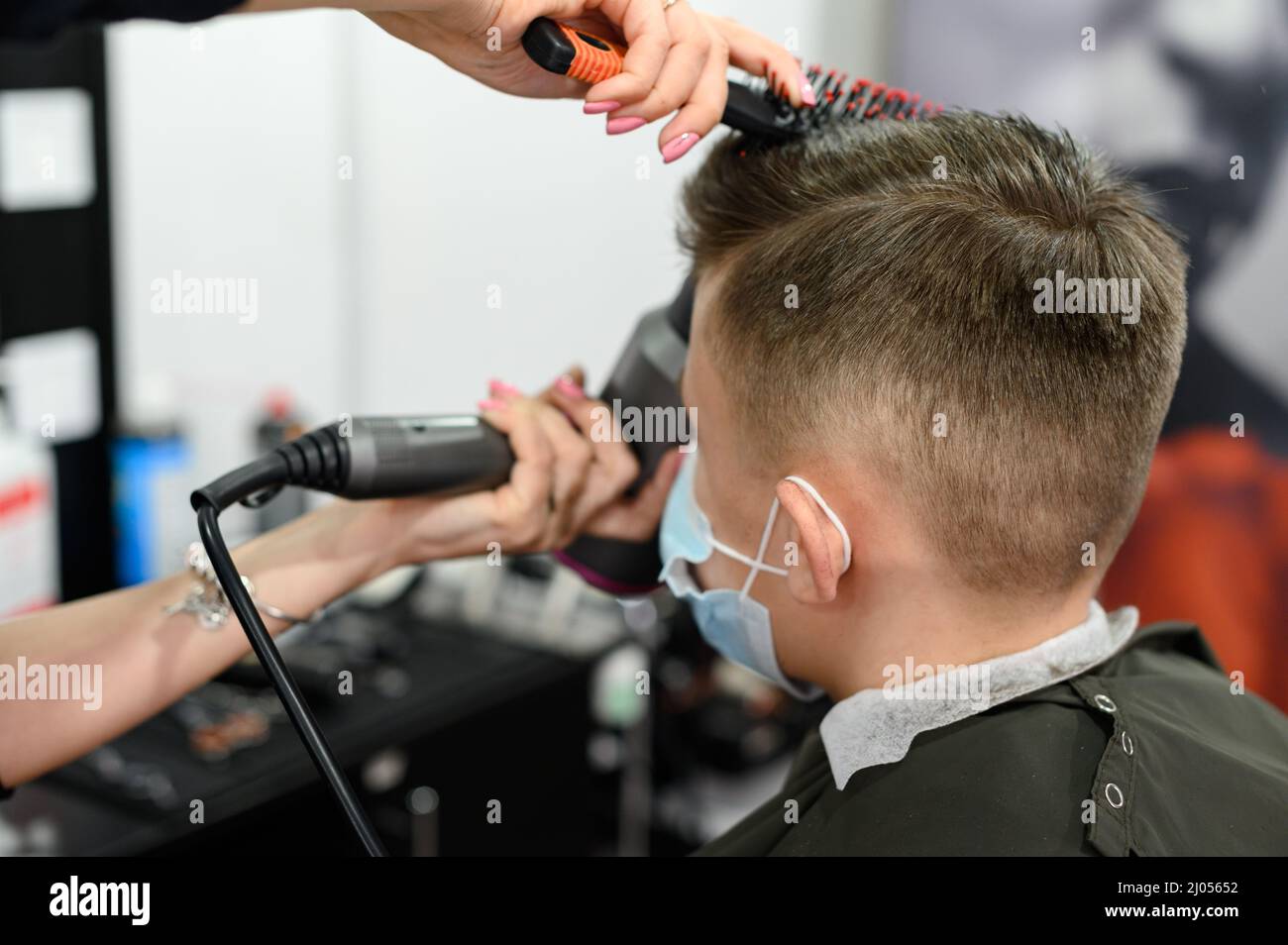 Il parrucchiere mette i capelli al ragazzo teen dopo il taglio dei capelli,  il taglio dei capelli per l'adolescente, l'acconciatura con un  asciugacapelli e una spazzola per capelli Foto stock - Alamy