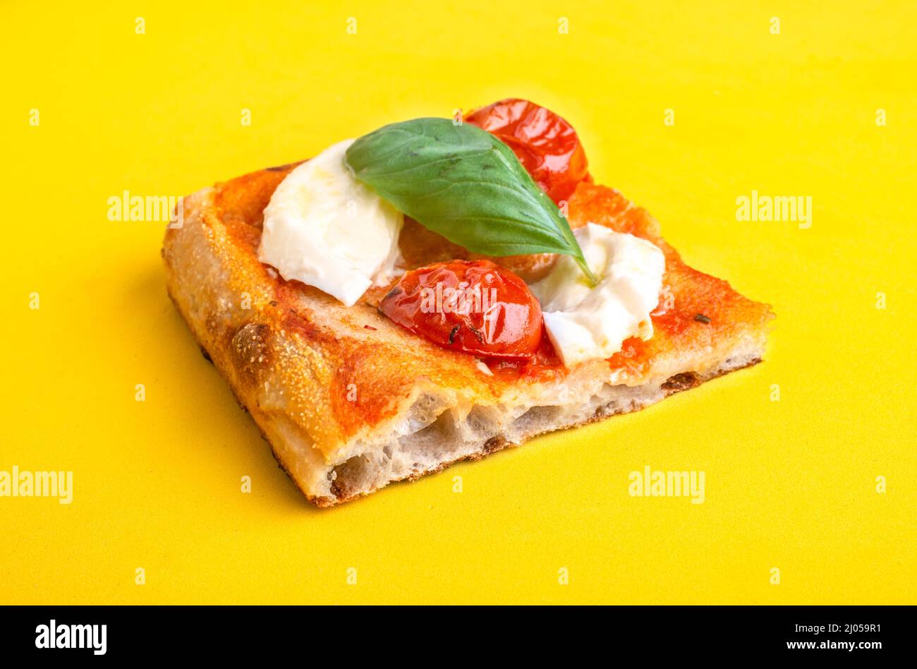 Un pezzo di pizza al taglio con pomodoro e mozzarella isolato su sfondo giallo Foto Stock