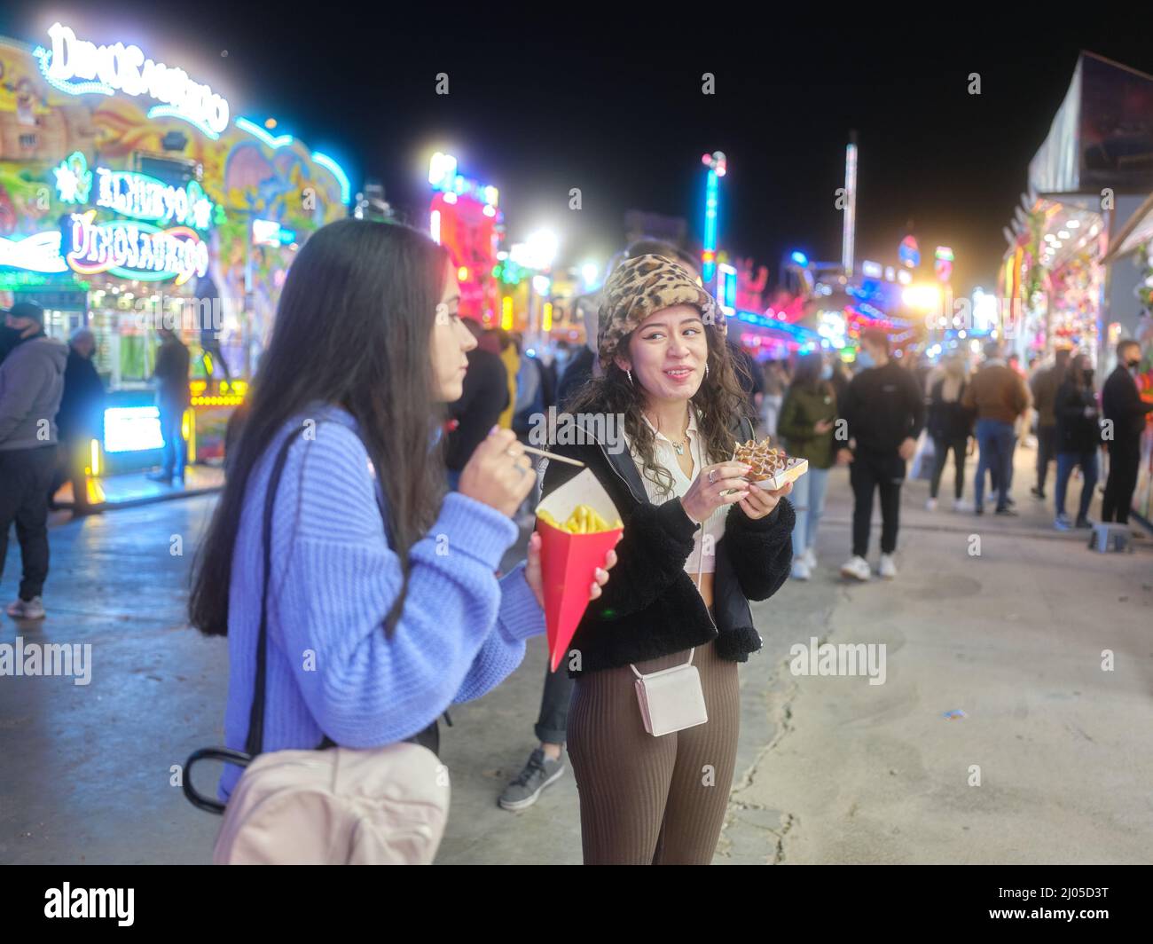 Due amici che mangiano fast food durante una fiera notturna Foto Stock