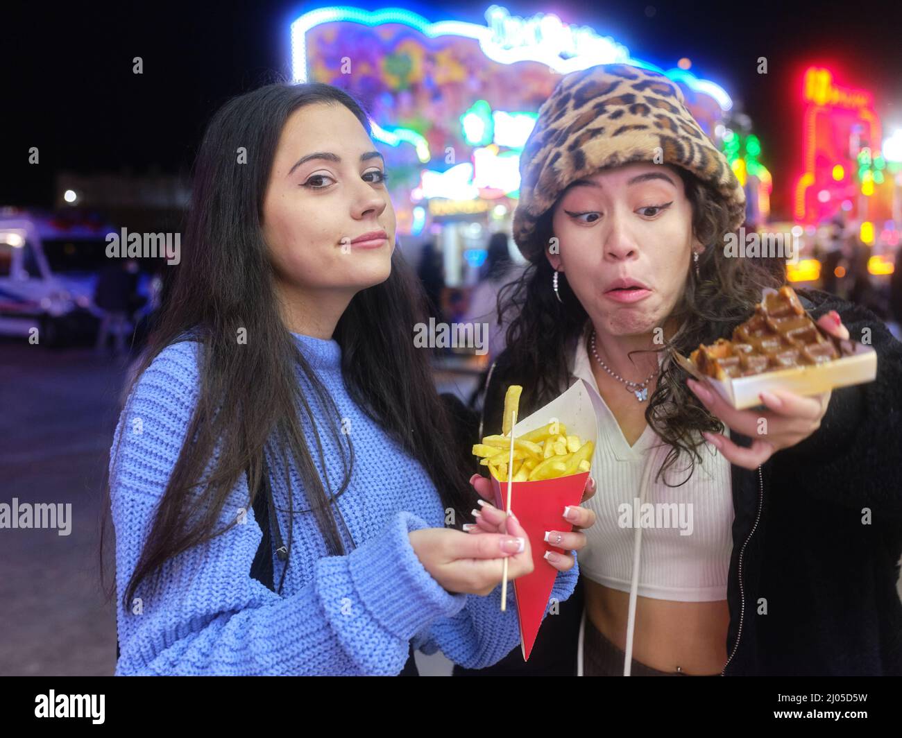 Donna esitantamente guardando un waffle accanto ad un amico con patatine fritte in una fiera di notte Foto Stock