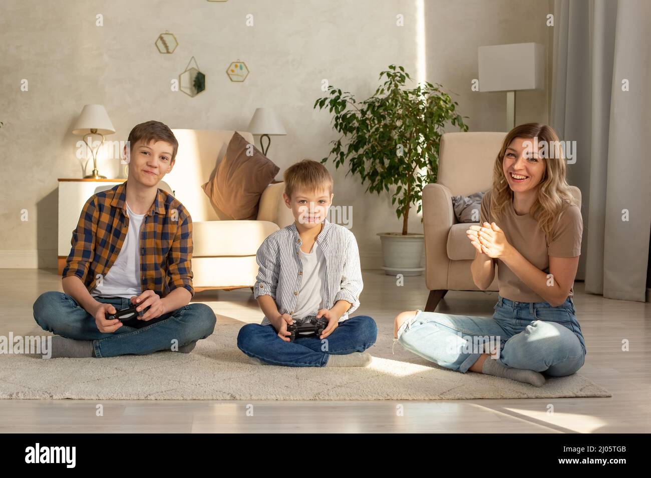 Ritratto di due ragazzi e donna felice si siede sul pavimento in una stanza che gioca video giochi con joystick Foto Stock