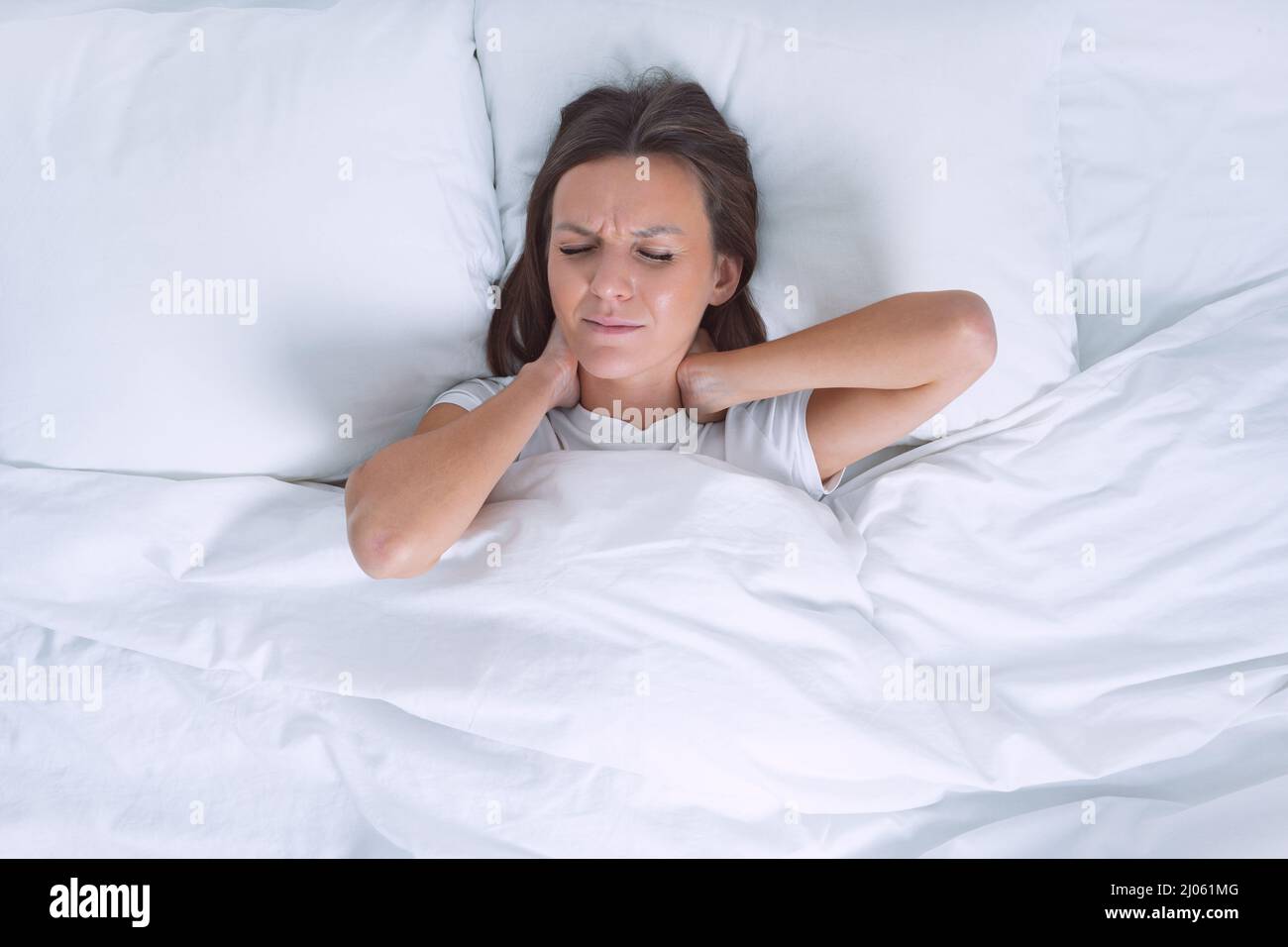 Donna a letto che soffre di dolore al collo al mattino dopo aver dormito su un cuscino scomodo. Dolore al collo, condrosi cervicale o osteocondrosi Foto Stock