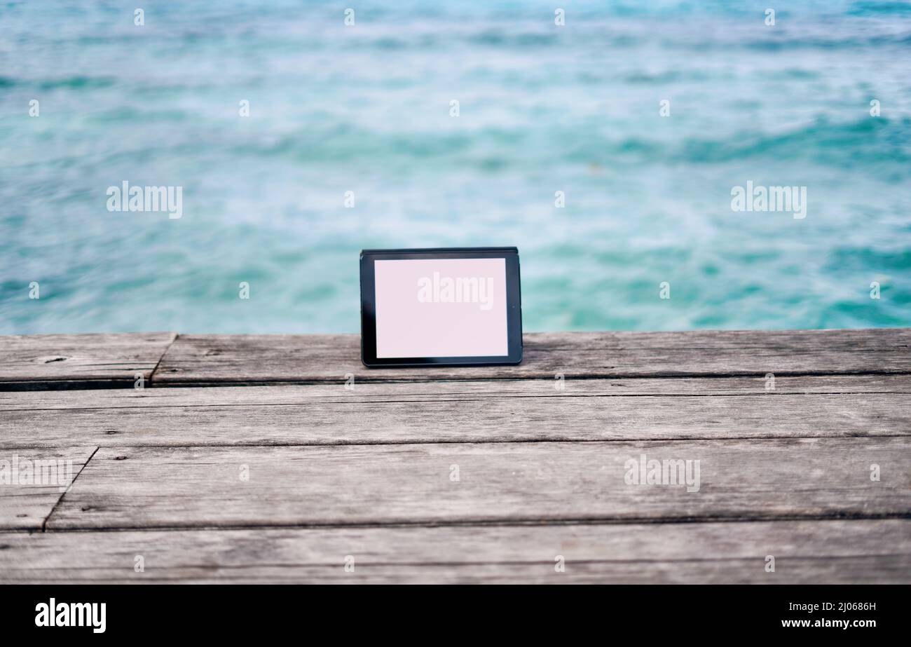 Resta in giro ovunque ti trovi nella vita. Foto di vita di un tablet digitale posto su una passerella che si affaccia sull'oceano in Raja Ampat, Indonesia Foto Stock