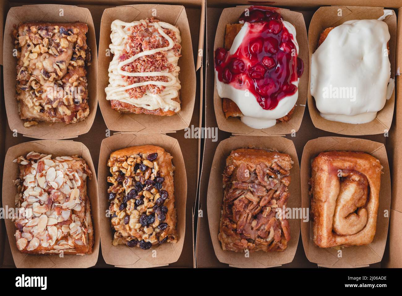 Scatola di dolci alla cannella freschi assortiti da forno da vicino, piatto. Noce, uva passa, mandorla, pecan, bacon d'acero, farciture di formaggio cremoso Foto Stock