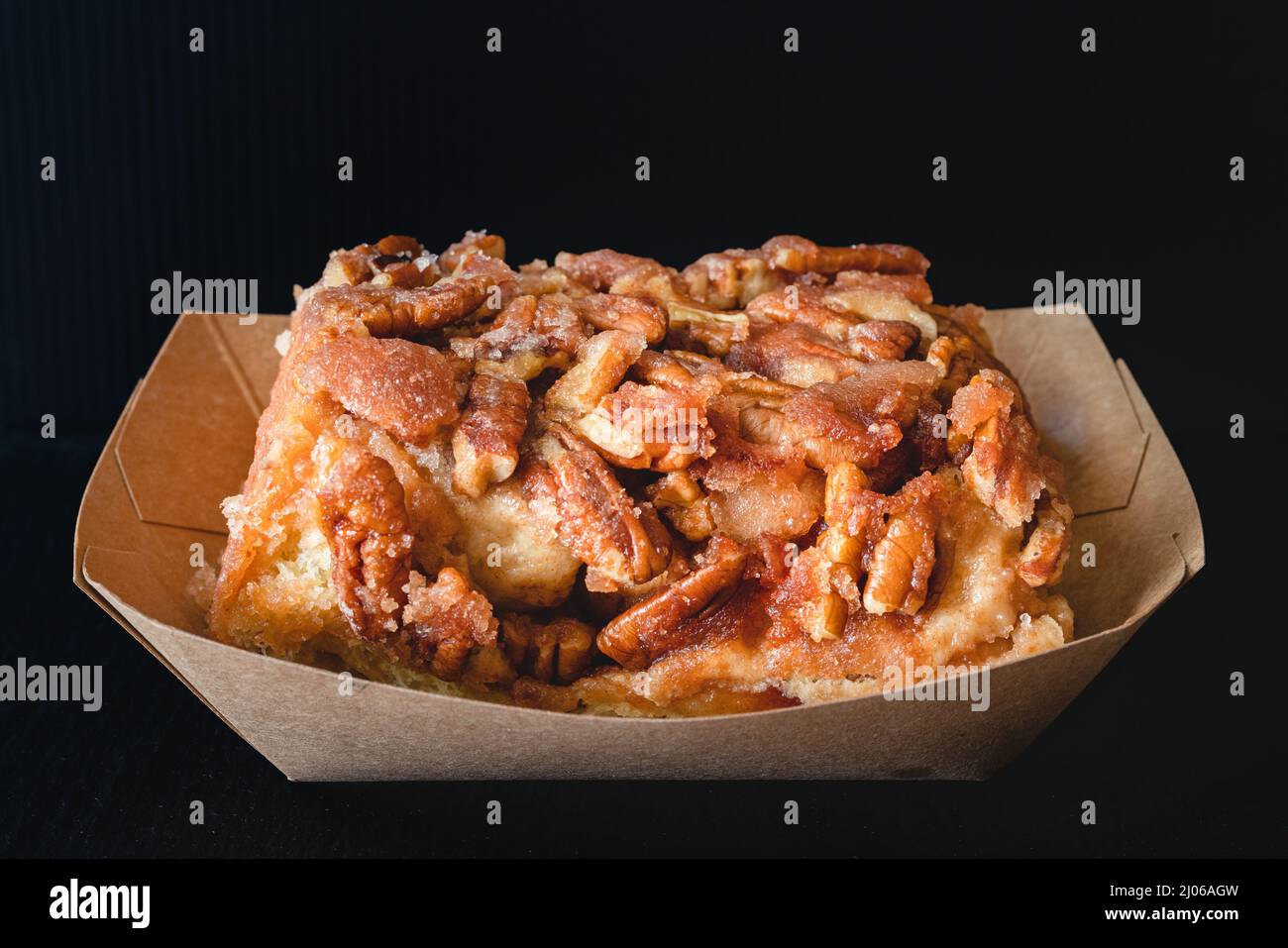 Rotolo di cannella ghiacciato Pecan da vicino su sfondo nero Foto Stock