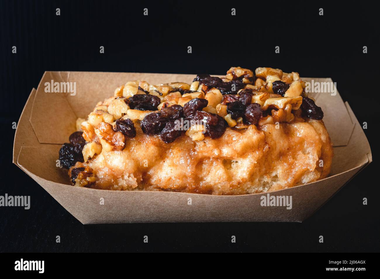 Raisin Noce Frosted Cinnamon roll da vicino su sfondo nero Foto Stock