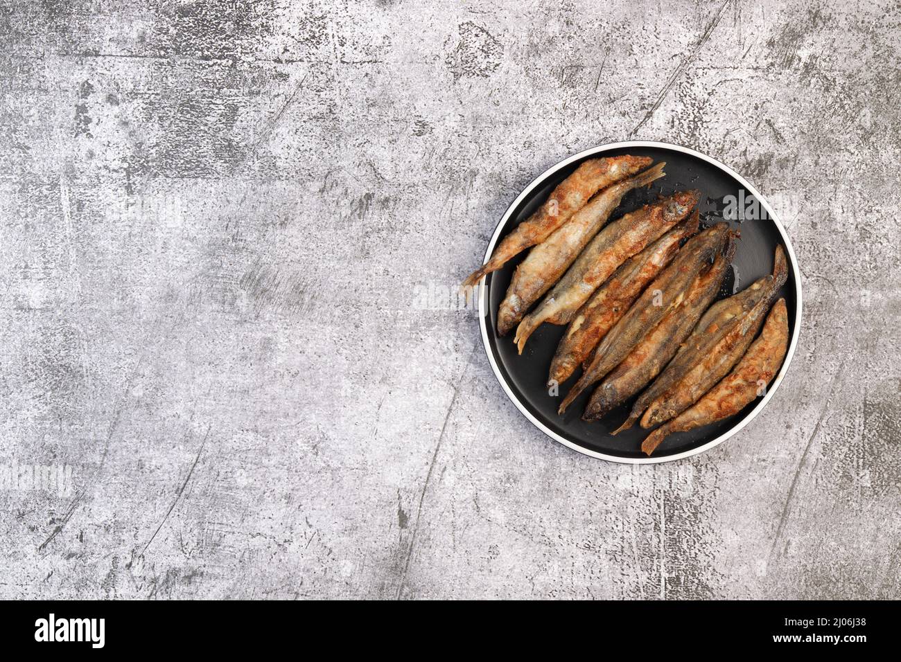 Pan il capelin fritto o il pesce odorato su un piatto rotondo su uno sfondo grigio scuro. Vista dall'alto, disposizione piatta Foto Stock