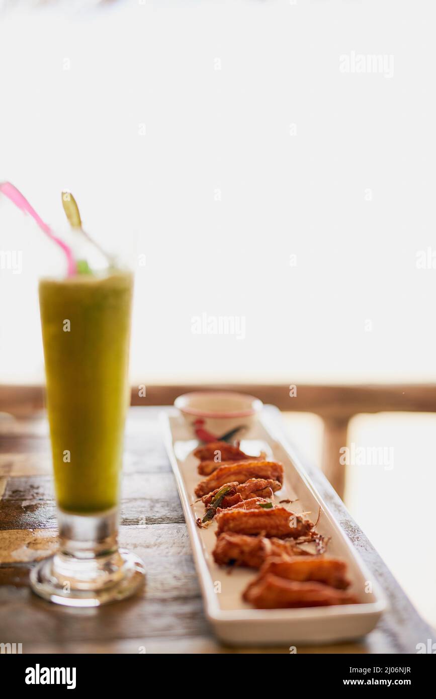 Tutto va bene con le ali. Shot di ali di pollo e un frullato seduto su un tavolo in un ristorante sul mare in Thailandia. Foto Stock