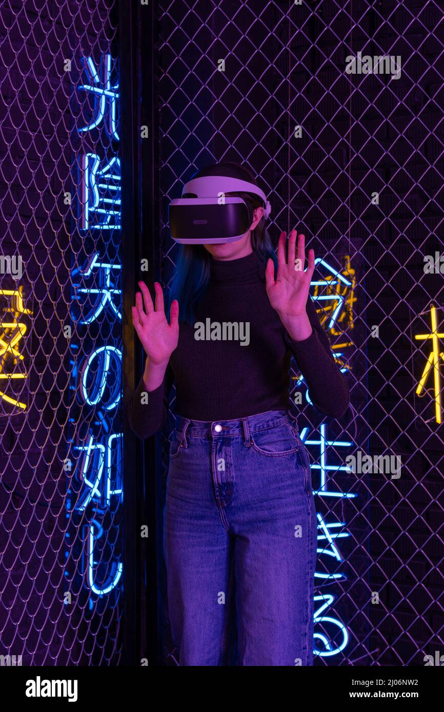 La teen girl che utilizza il visore vr è in realtà virtuale il futuristico neon futuristico sfondo colorato del cyberspazio. Il concetto di metaverse, realtà virtuale, virtua Foto Stock