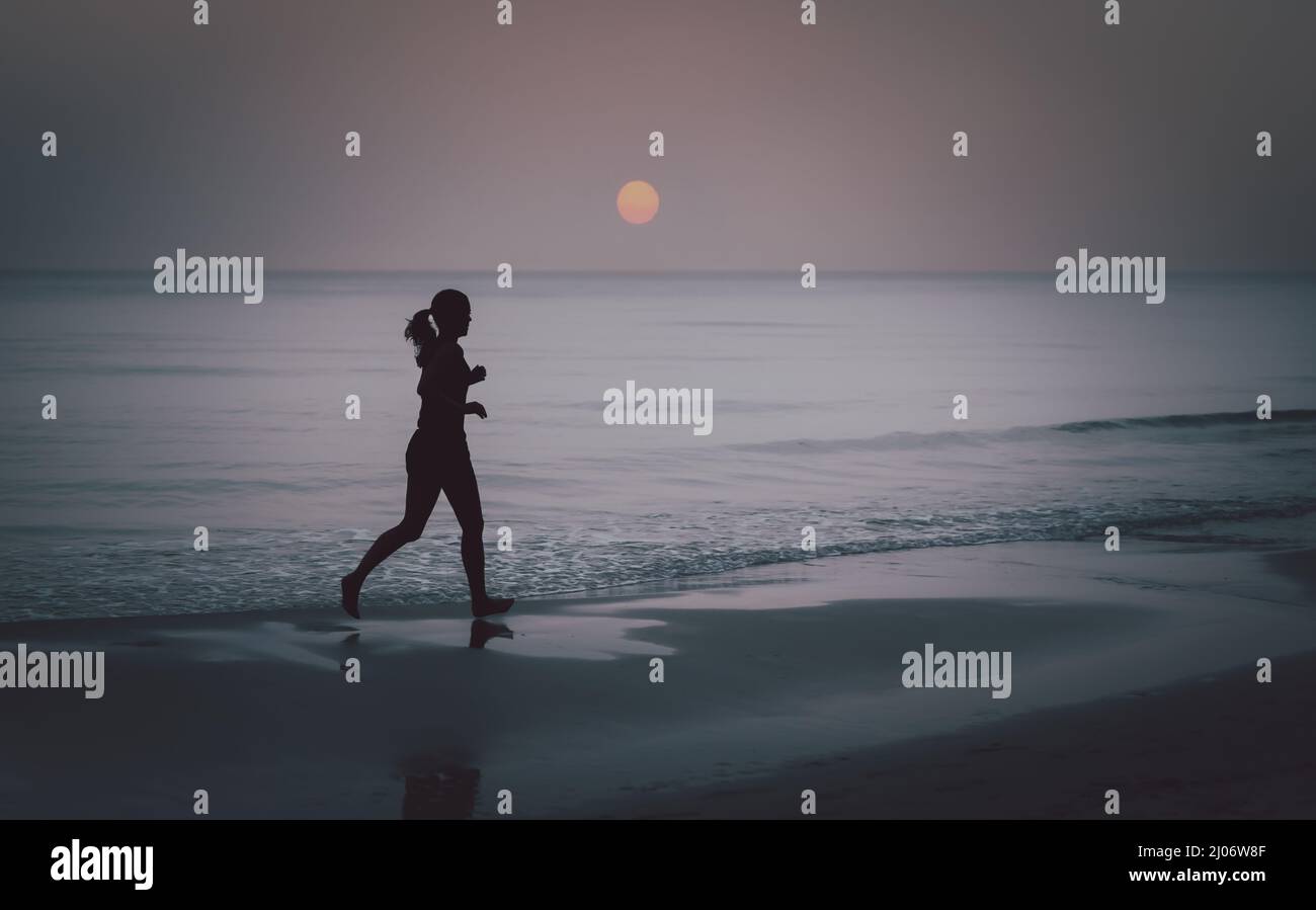Silhouette di donna a piedi nudi che corre sulla spiaggia all'alba. Foto Stock