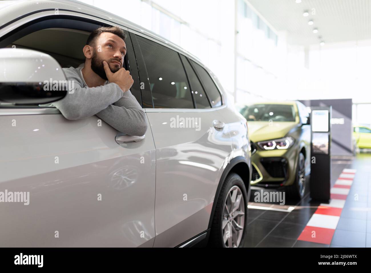 Un acquirente in una concessionaria di auto si siede in un SUV e pensa all'acquisto e all'assicurazione di una nuova auto Foto Stock