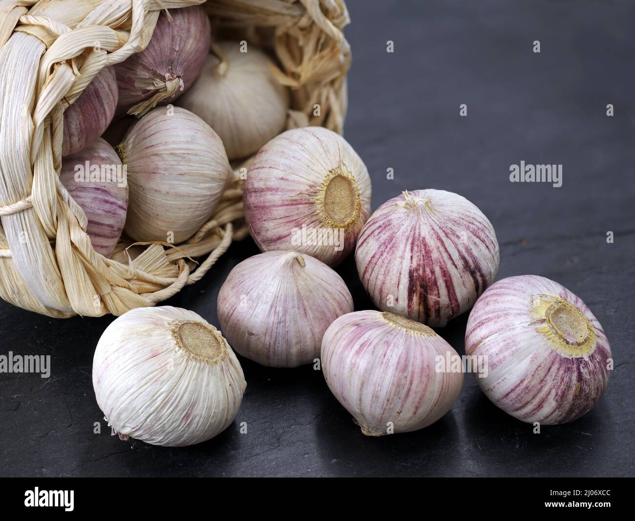 Solo aglio o aglio cinese, Allium sativum in un cestino di paglia su sfondo nero ardesia Foto Stock