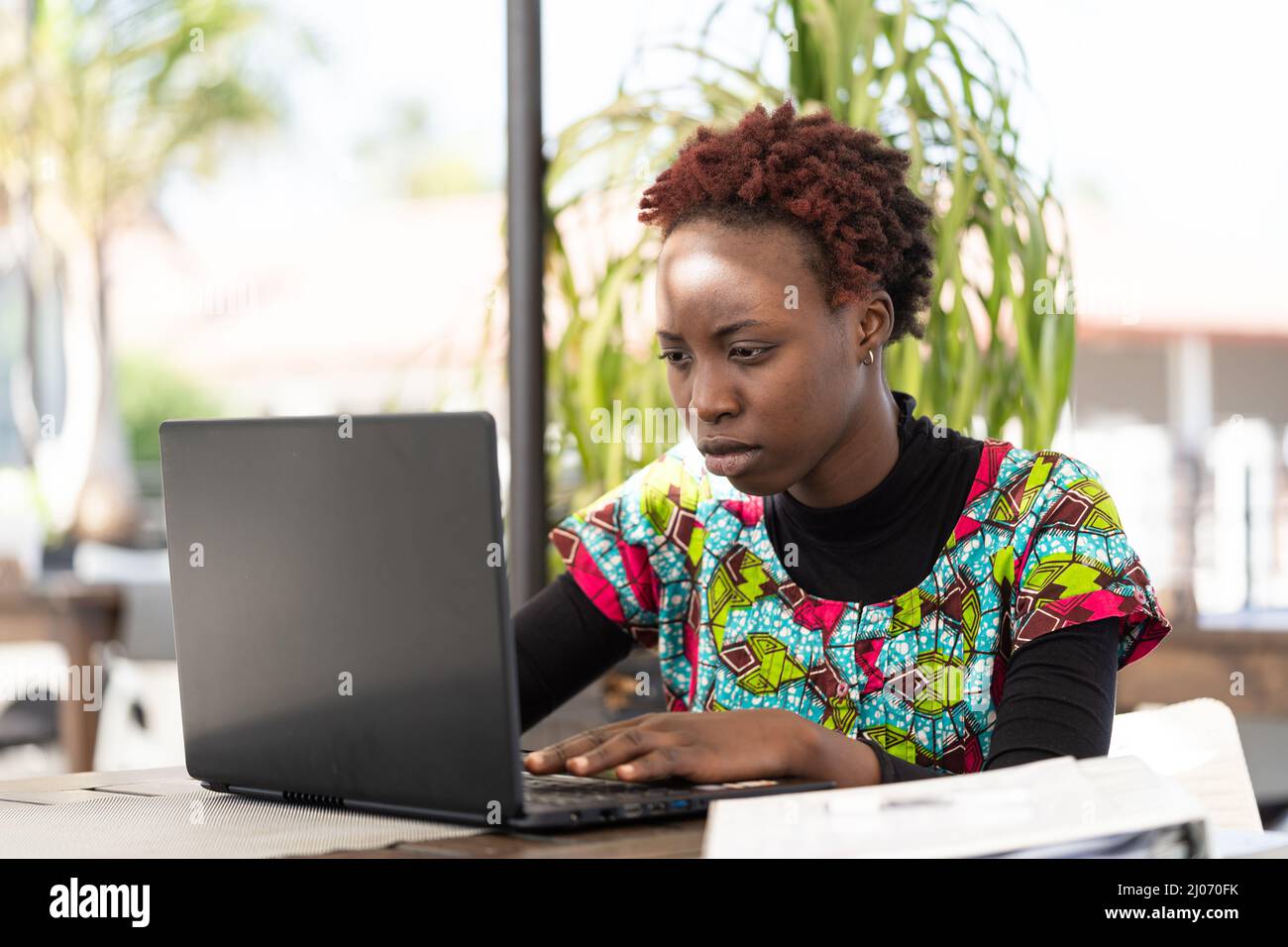 Seria giovane ragazza africana seduta al suo portatile e alla ricerca di un lavoro su internet; problema sociale della disoccupazione giovanile nei paesi in via di sviluppo Foto Stock