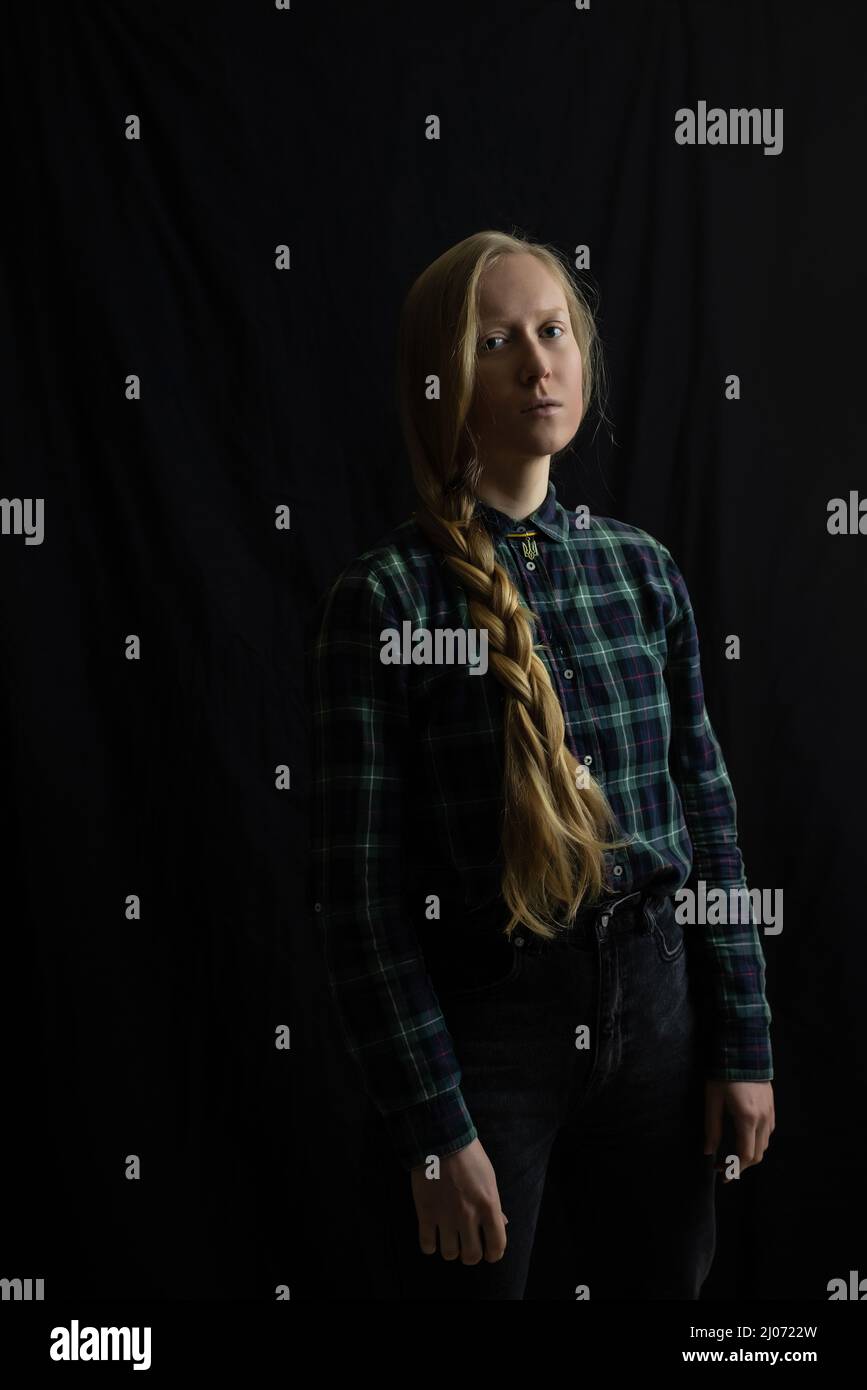 Una giovane donna Ucraina bionda con una treccia intrecciata in studio su uno sfondo nero isolato e un pendente Trident. Il concetto di fermare la guerra in Ucraina dagli invasori russi Foto Stock