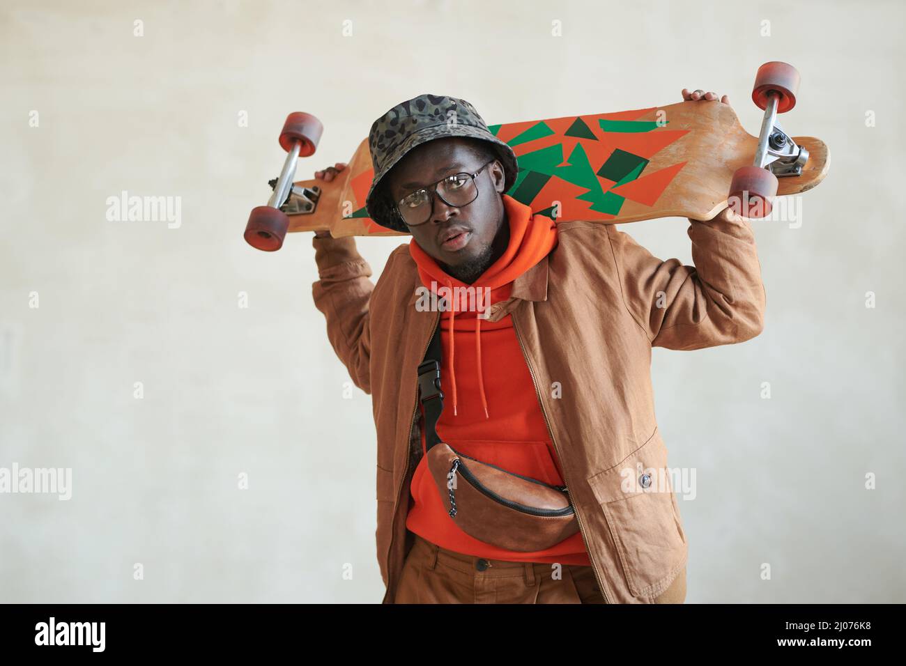 Ritratto orizzontale medio studio di bel ragazzo afroamericano vestito casual in posa su fotocamera con skateboard, spazio copia Foto Stock