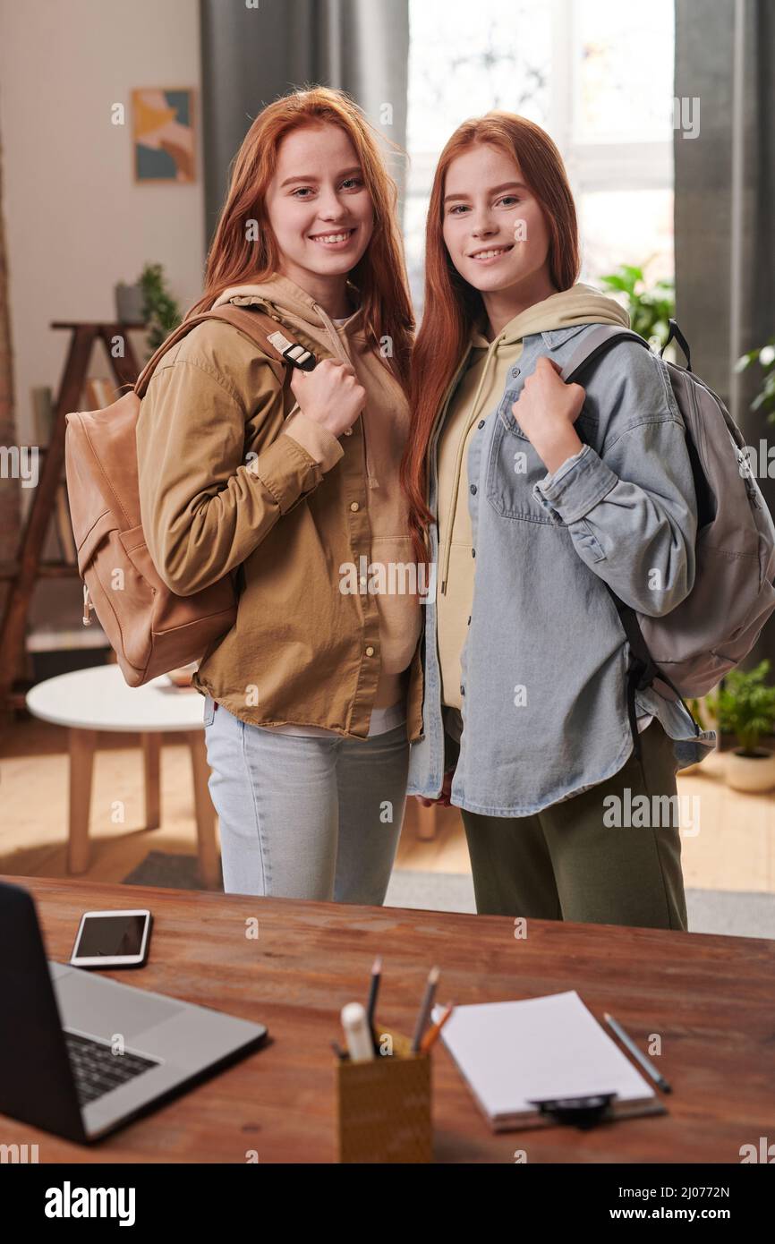 Ritratto medio lungo di studenti universitari moderni gemelli con abiti casual e zaini in piedi in salotto pronto per andare a scuola Foto Stock