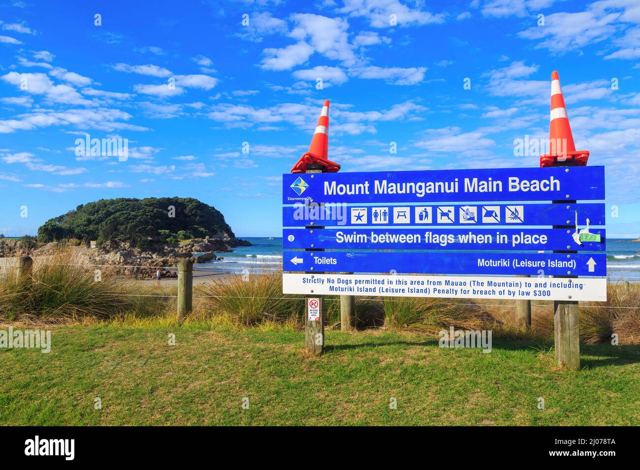 Un cartello 'Mount Maunganui Main Beach' sul Monte Maunganui, Nuova Zelanda, 'decorato' con coni stradali. Sullo sfondo c'è l'Isola di Moturiki Foto Stock