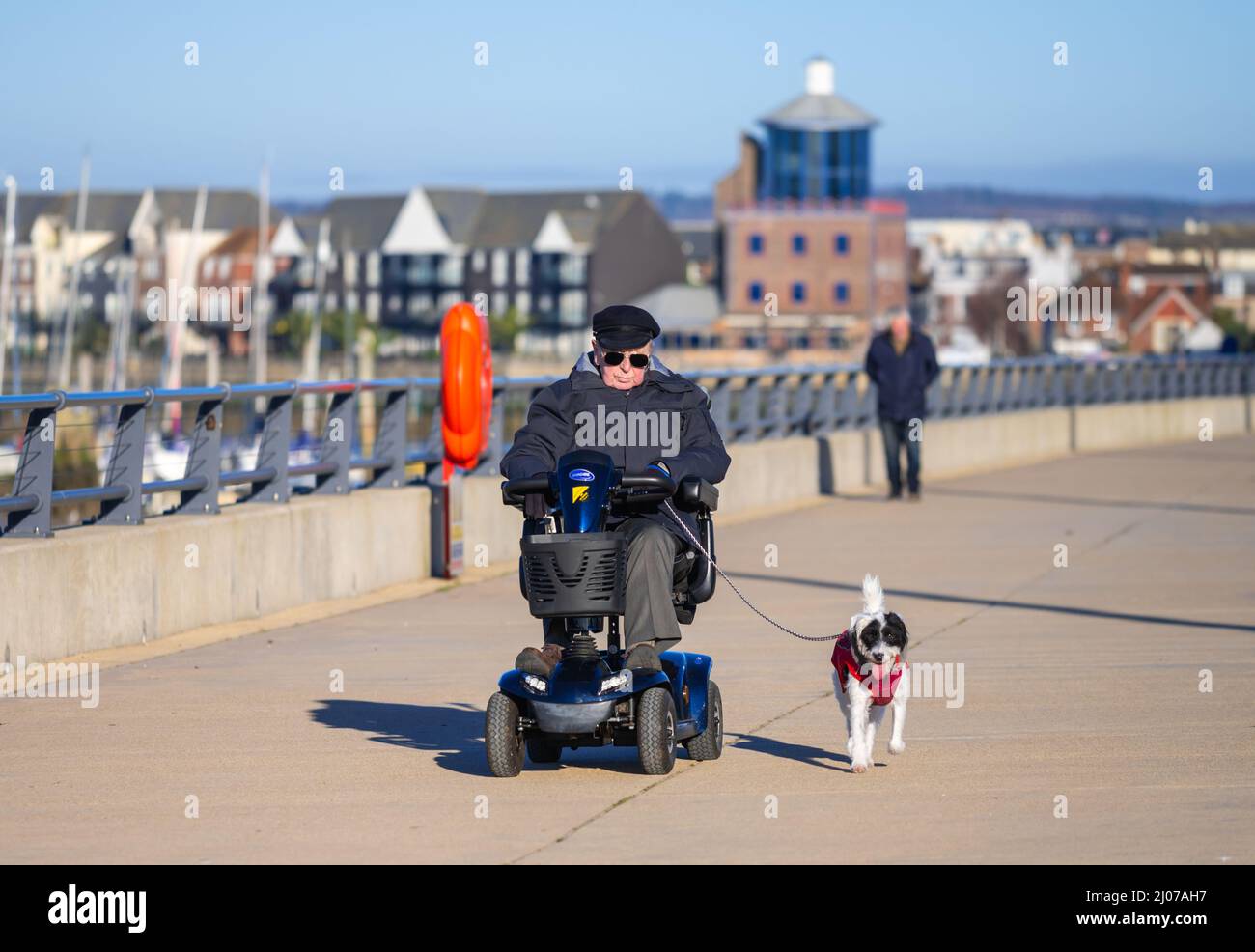 Uomo anziano in uno scooter di mobilità che cammina un cane su un cavo lungo un alzaia lungo il fiume nel Regno Unito. Foto Stock
